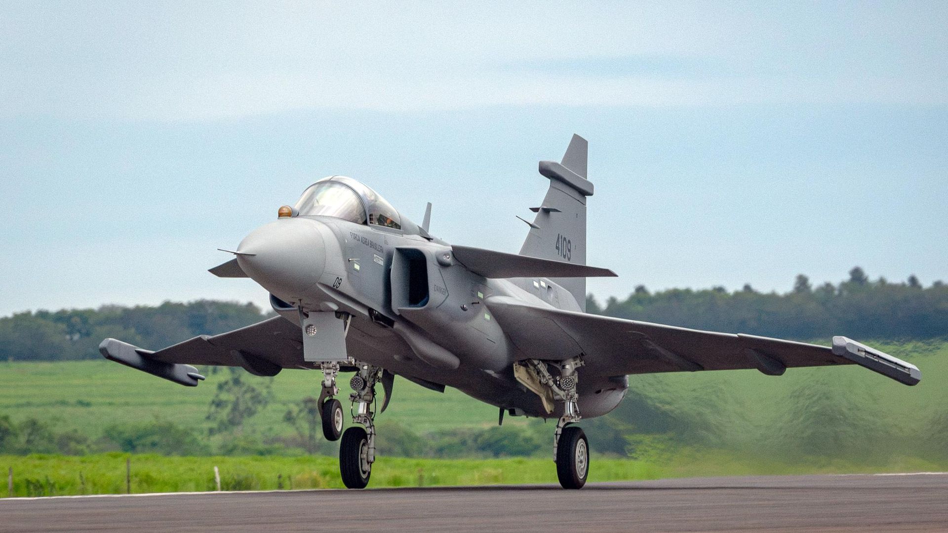 A fighter jet with markings "Força Aérea Brasileira" on a runway with nose gear visible.
