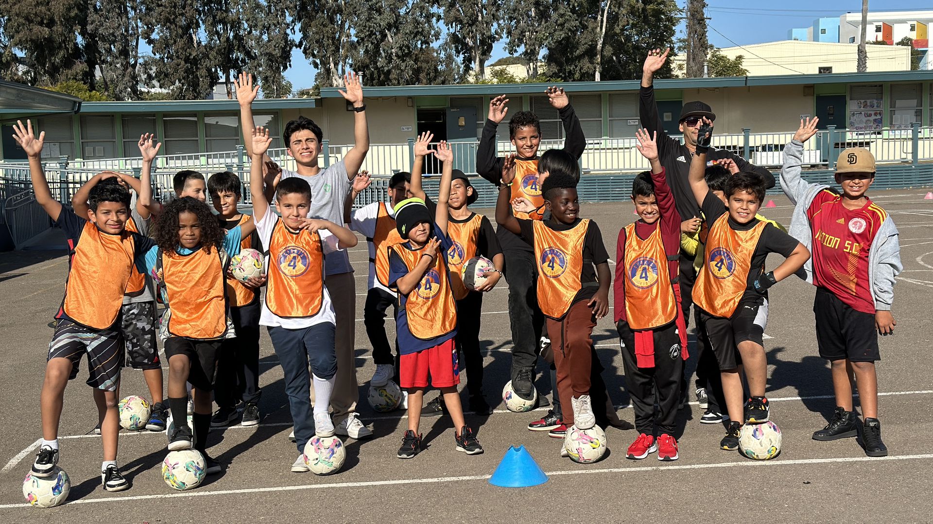 An adult coach and a teenage volunteer pose with elemntary school students playing soccer