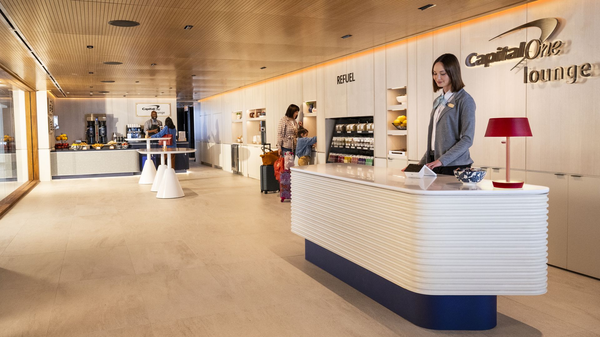 A woman stands behind a desk, with a sign reading "Capital One Lounge."