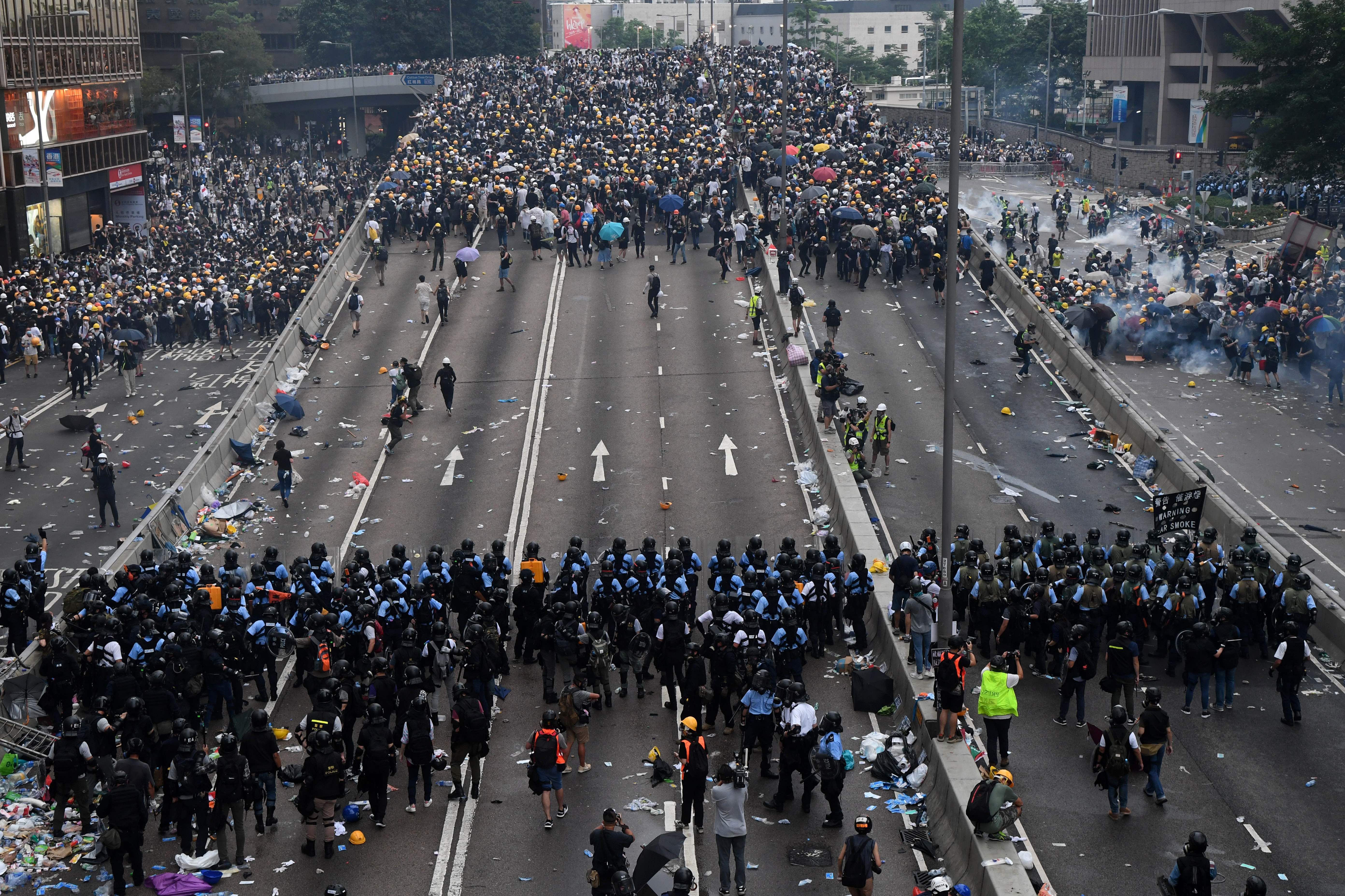 In this image, a line of protestors face a line of police on a road in Hong Kong.