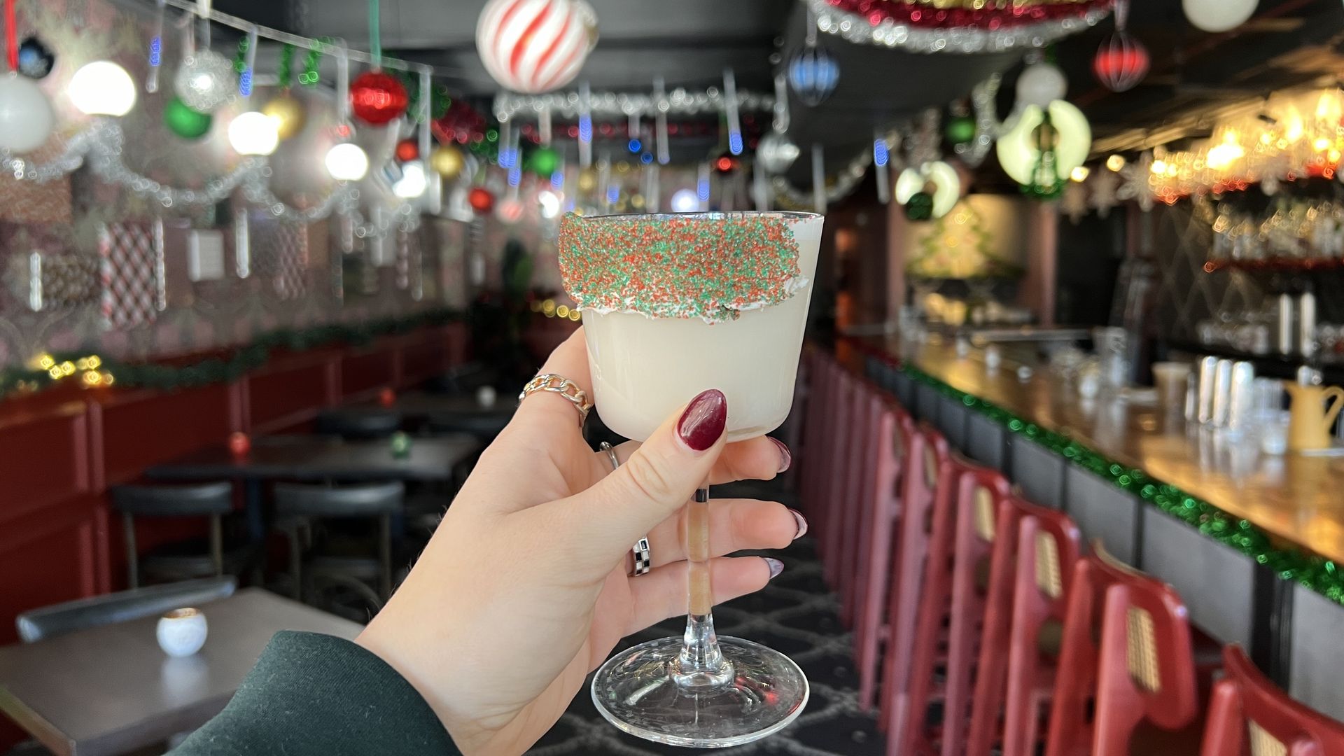 hand holding cocktial glass inside bar decorated for christmas