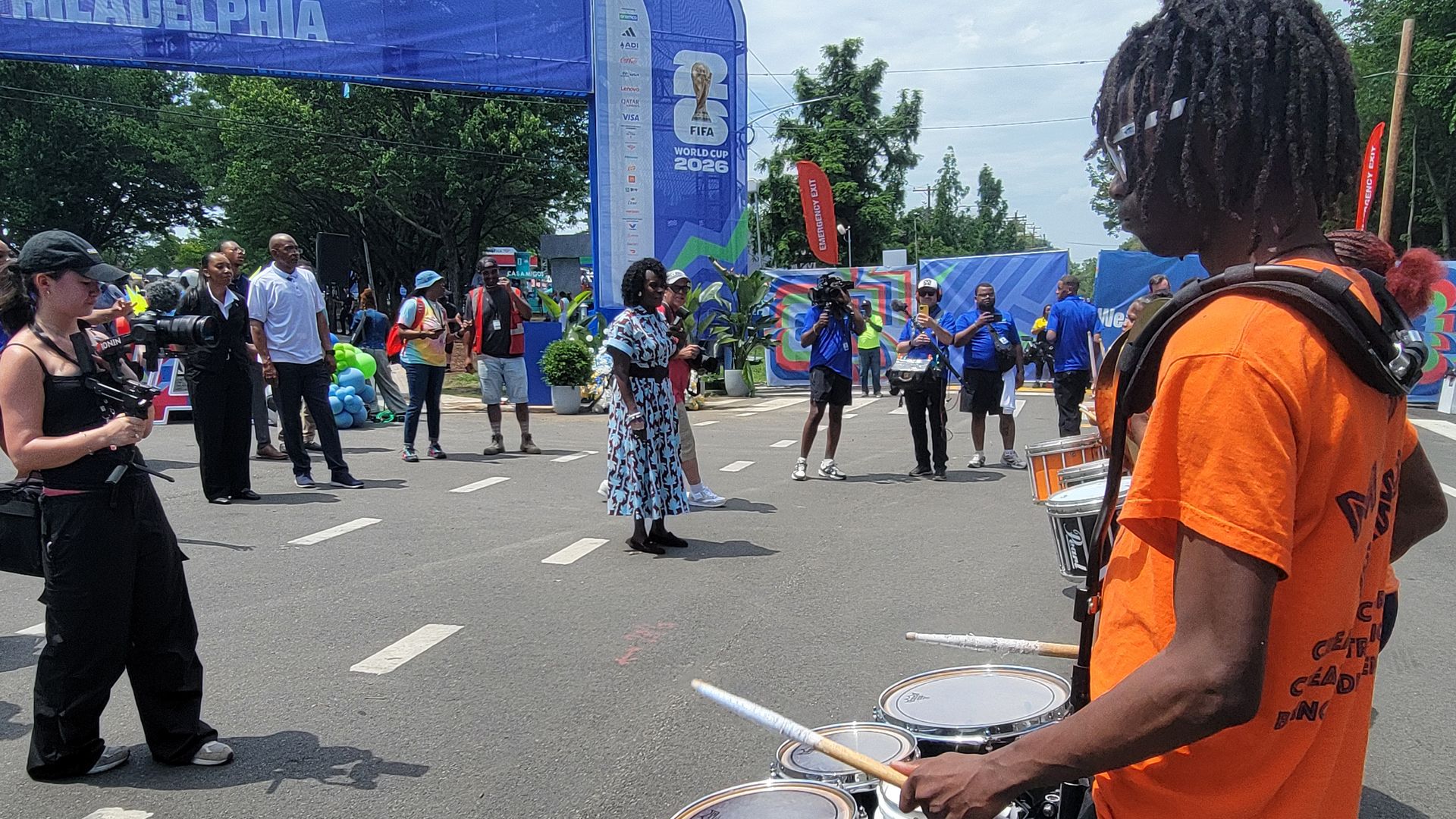 Street parade with drummers in orange on the right, Mayor Cherelle Parker in a blue floral dress walking center.