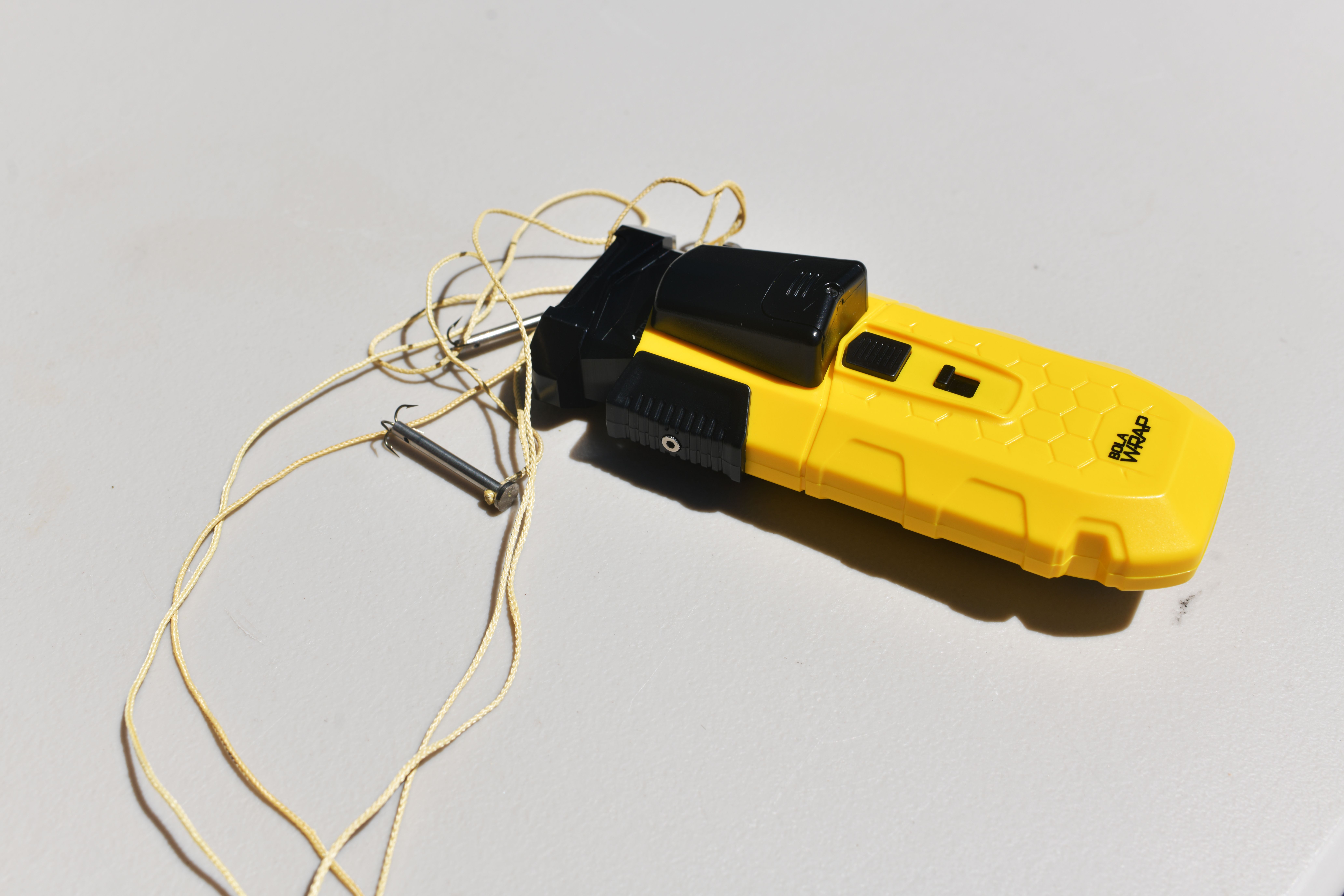 A bright yellow BolaWrap cartridge with the tether around it 