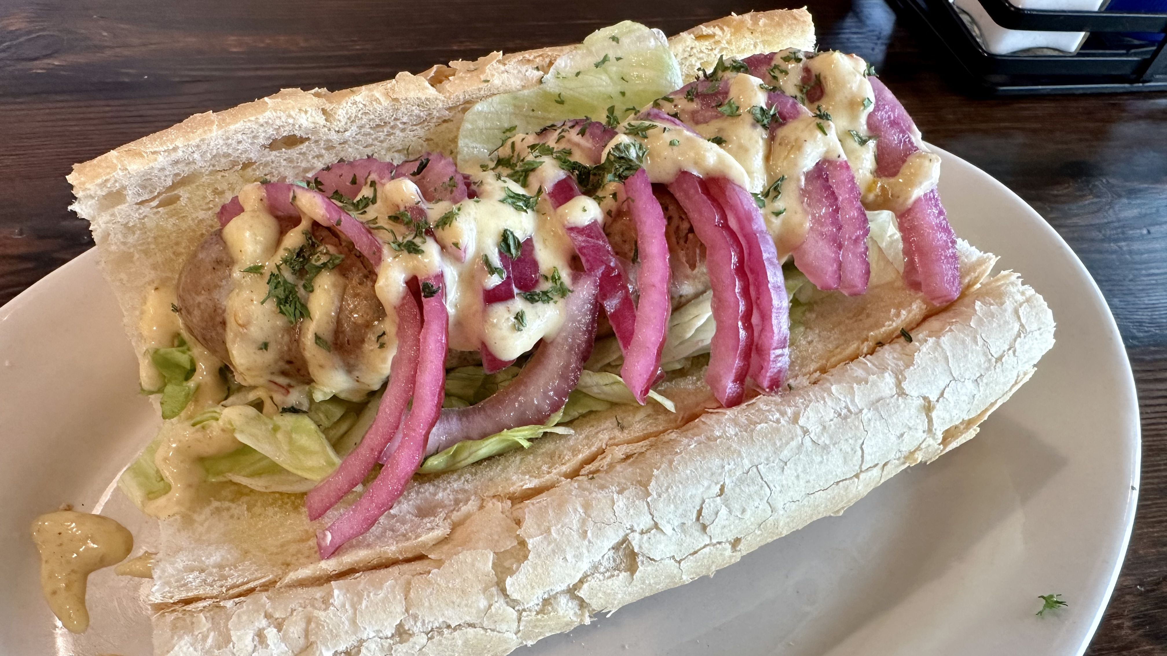 Photo shows a jerk chicken sausage poboy dressed with pickled red onions.