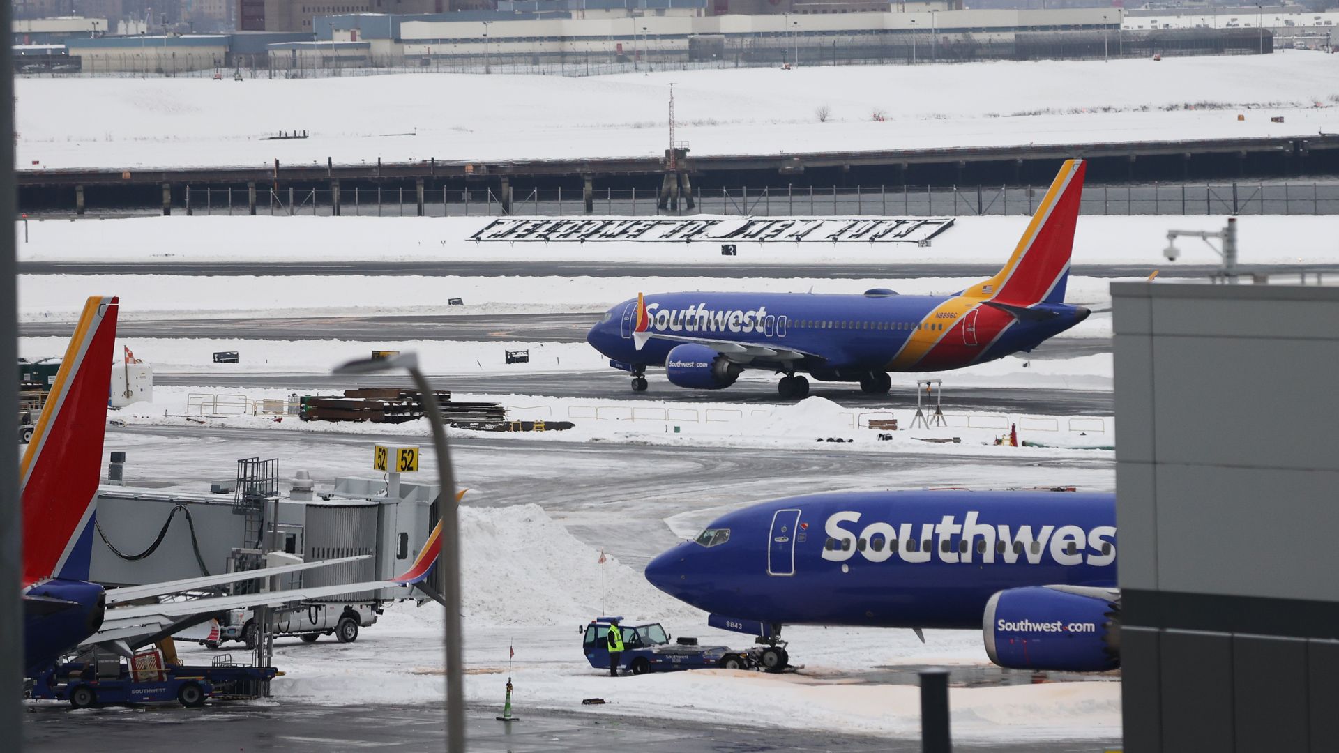 Snow-covered airport runway with three Southwest Airlines planes, a city skyline in the background, and a sign in snow reading "WELCOME TO NEW YORK."