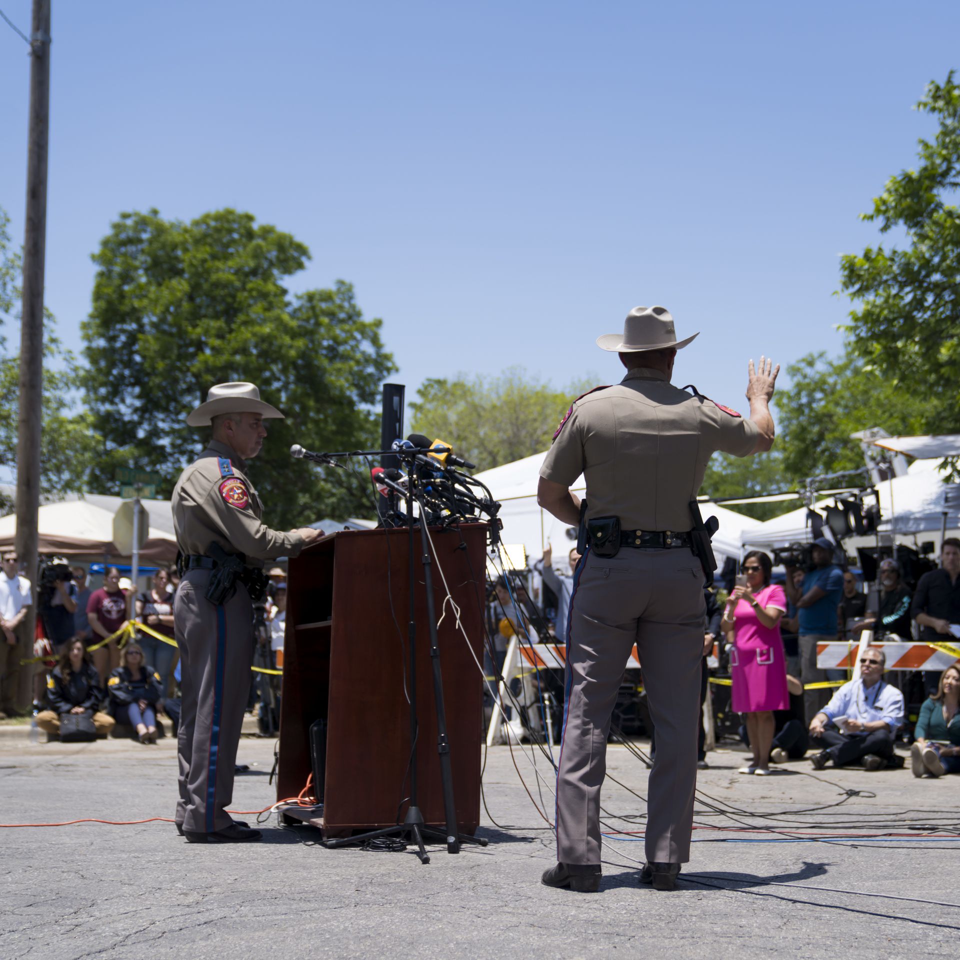 A Texas Department of Public Safety officer waves his hand at a throng of reporters while another one stands at a podium in front of several microphones