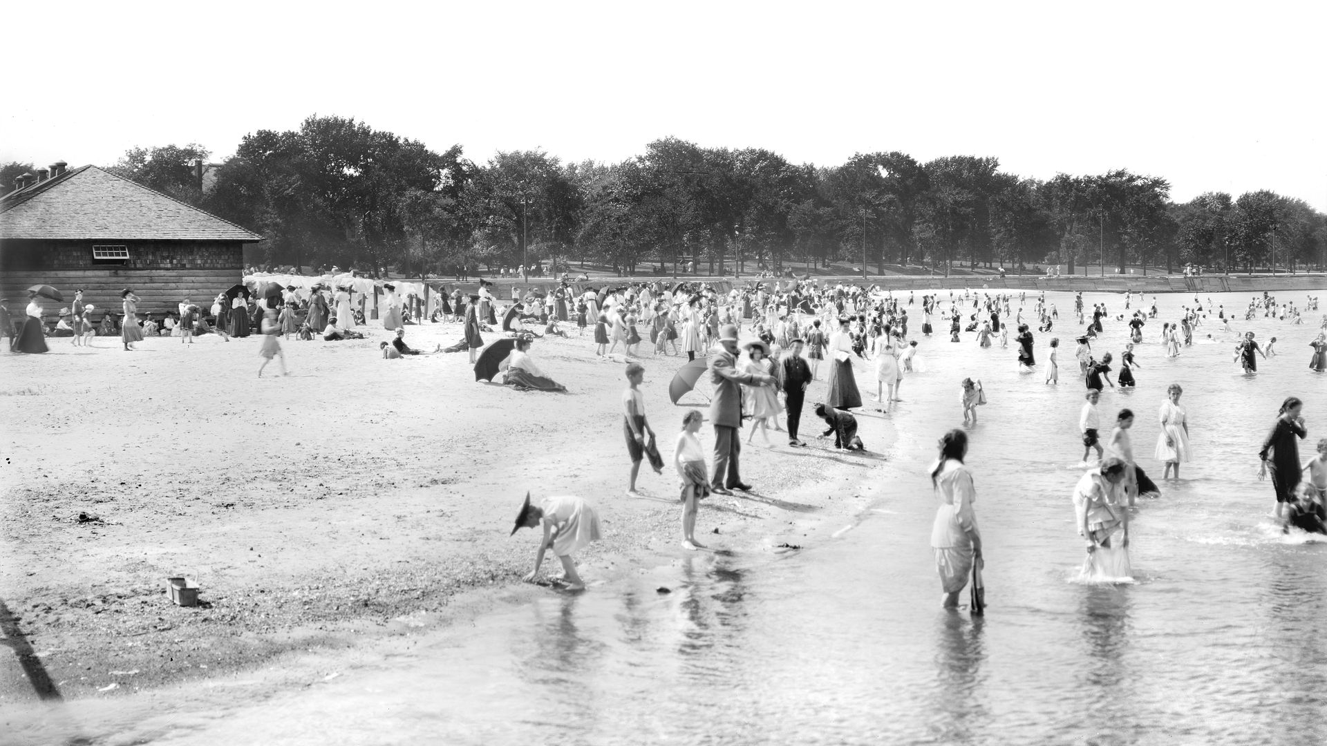 Photo of people standing in water at a beach. 