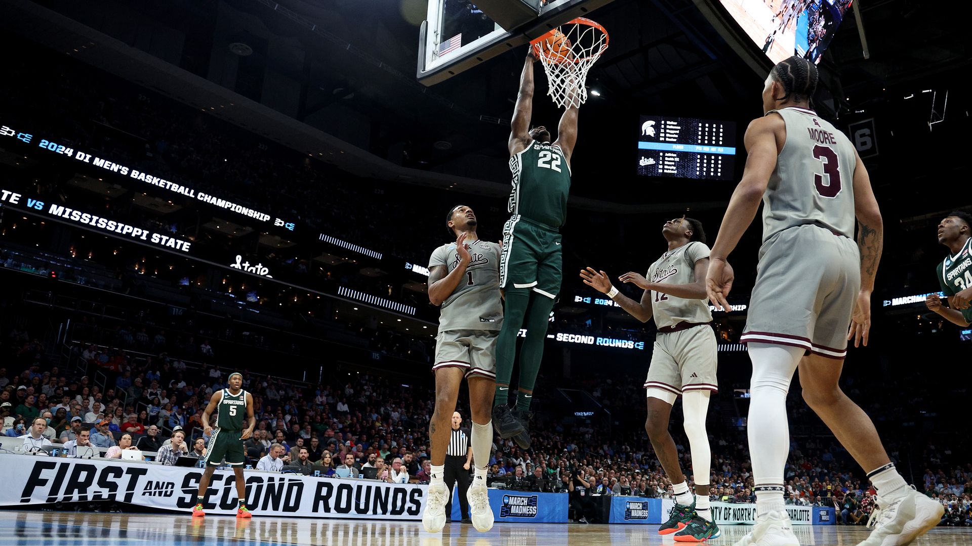 A basketball player in a green uniform dunks the ball surrounded by players in gray uniforms