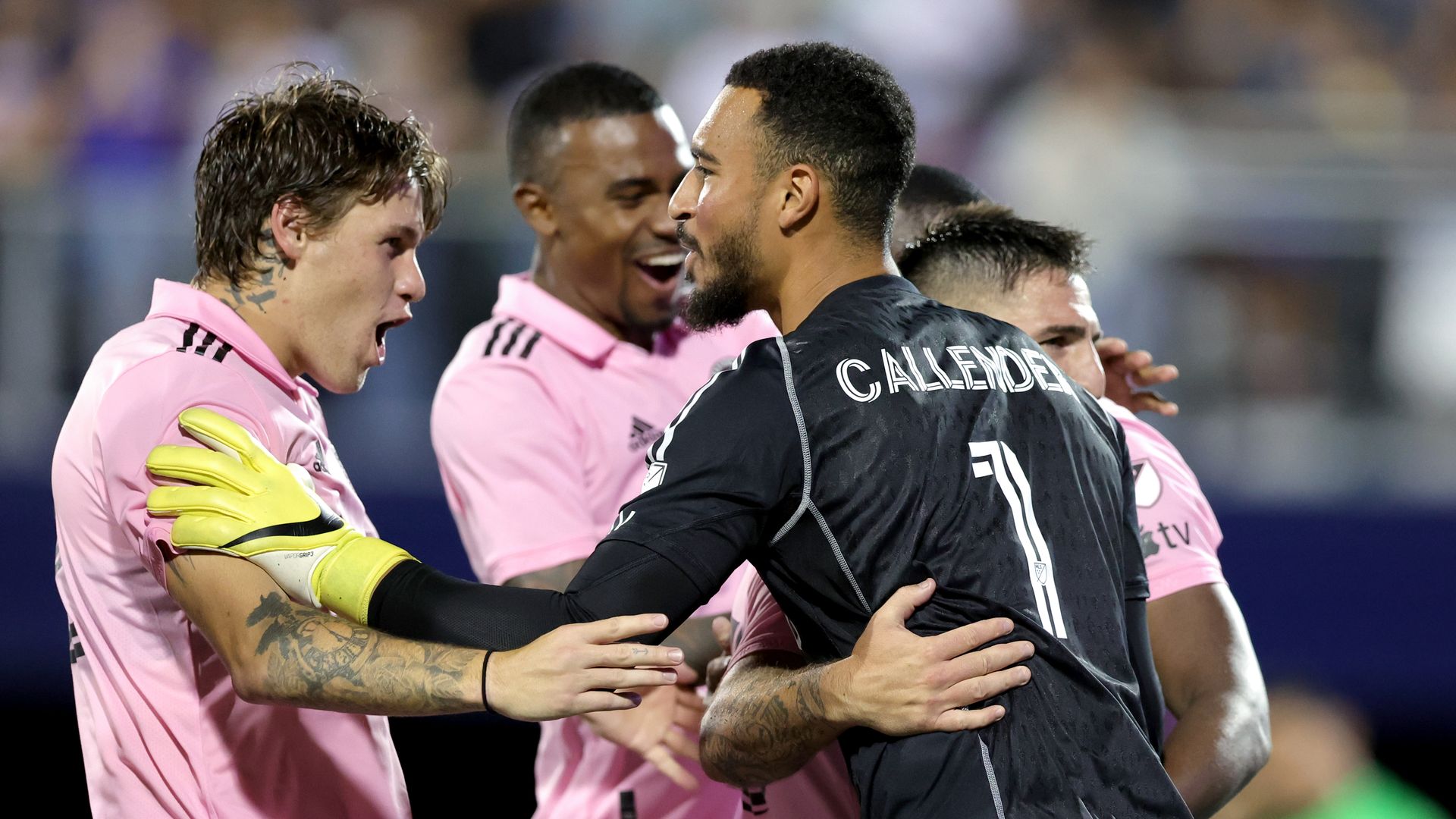 Drake Callender, in a black jersey, celebrates with teammates wearing pink jerseys. 