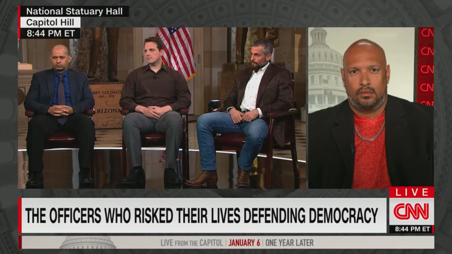 Screencap of an interview with three men sitting on the left and a separate window showing another man calling in virtually on the right