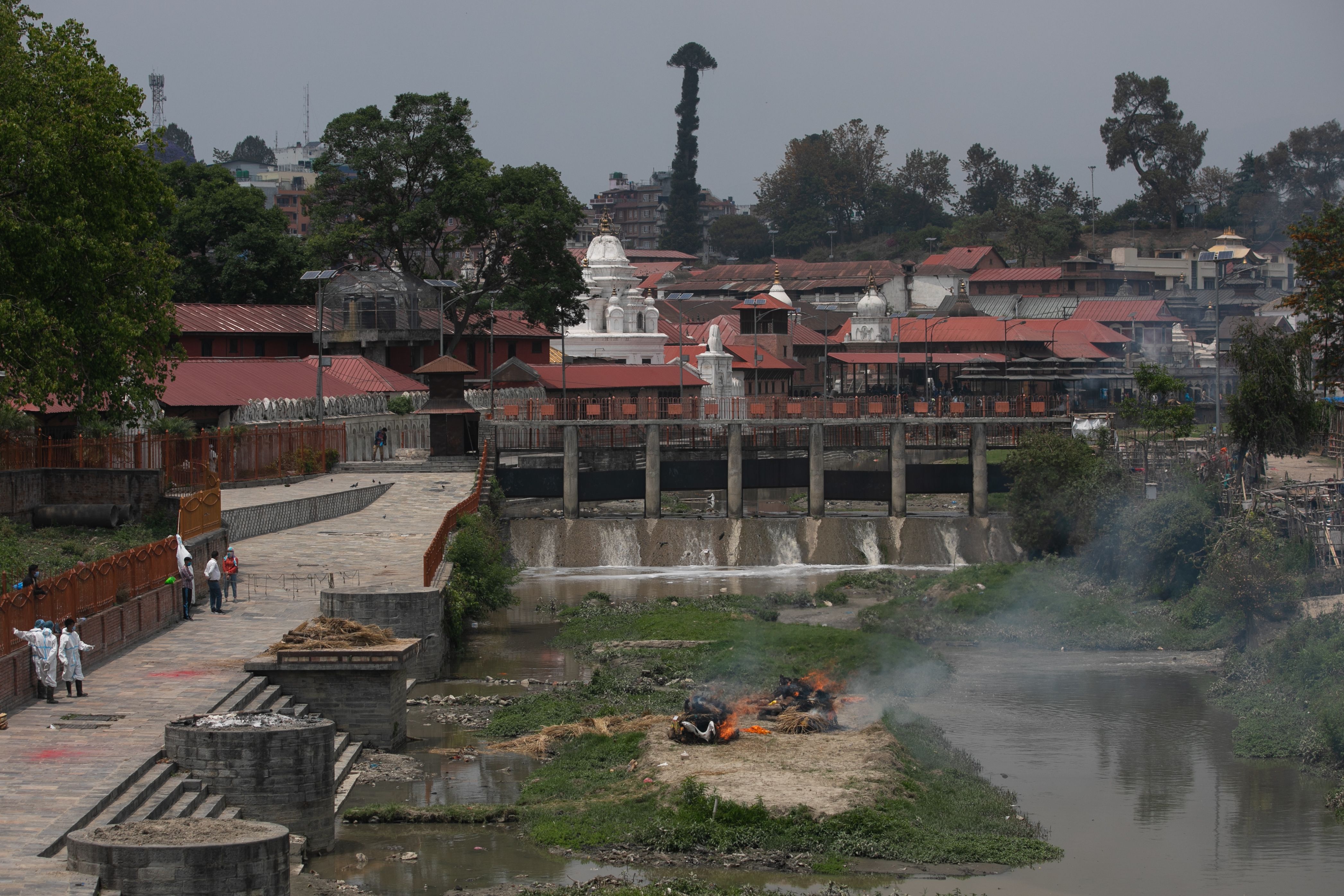 Nepalese workers wearing protective suits stand near the burning dead bodies of Coronavirus (COVID-19) victims during a cremation at the premises of Pashupatinath temple in Kathmandu. 