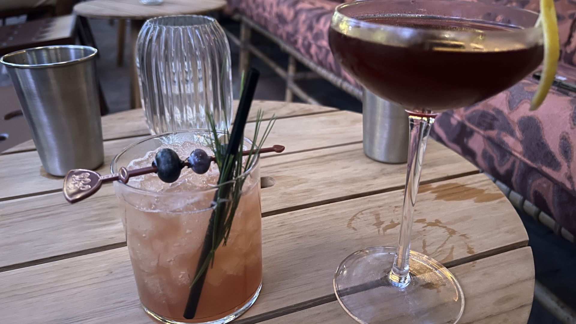 Two cocktails on an outdoor circular wooden table.