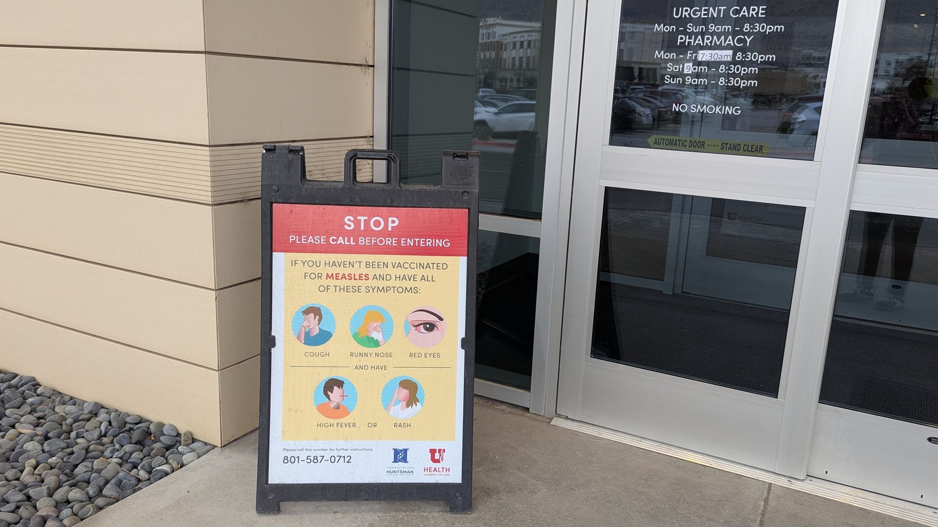 A sign outside of an urgent care clinic reads, "STOP // PLEASE CALL BEFORE ENTERING // IF YOU HAVEN'T BEEN VACCINATED FOR MEASLES AND HAVE ALL OF THESE SYMOTONS: COUGH, RUNNY NOSE, RED EYES // AND HAVE HIGH FEVER OR RASH