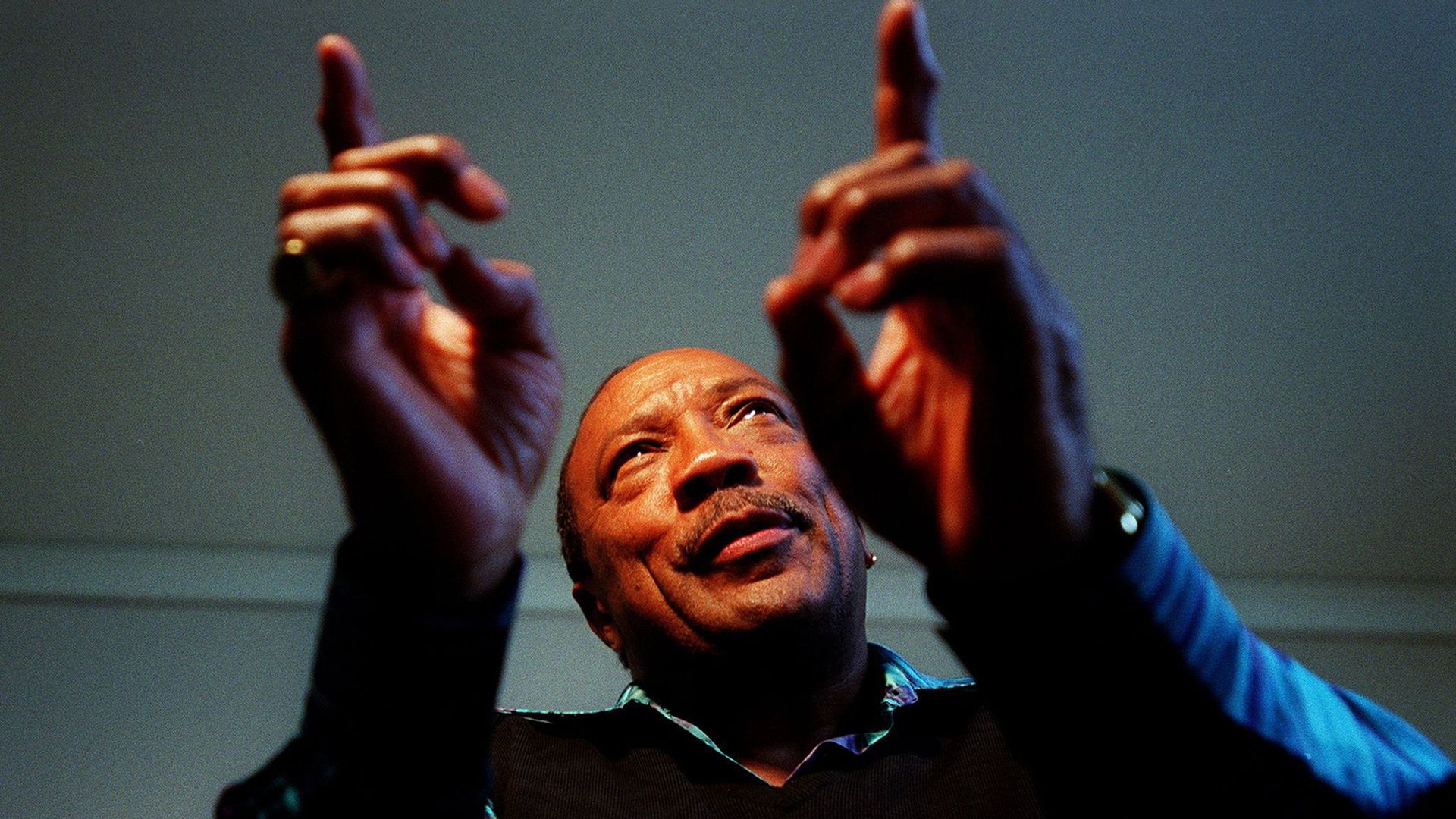 Quincy Jones in his older years holds up two fingers as he talks about music. 