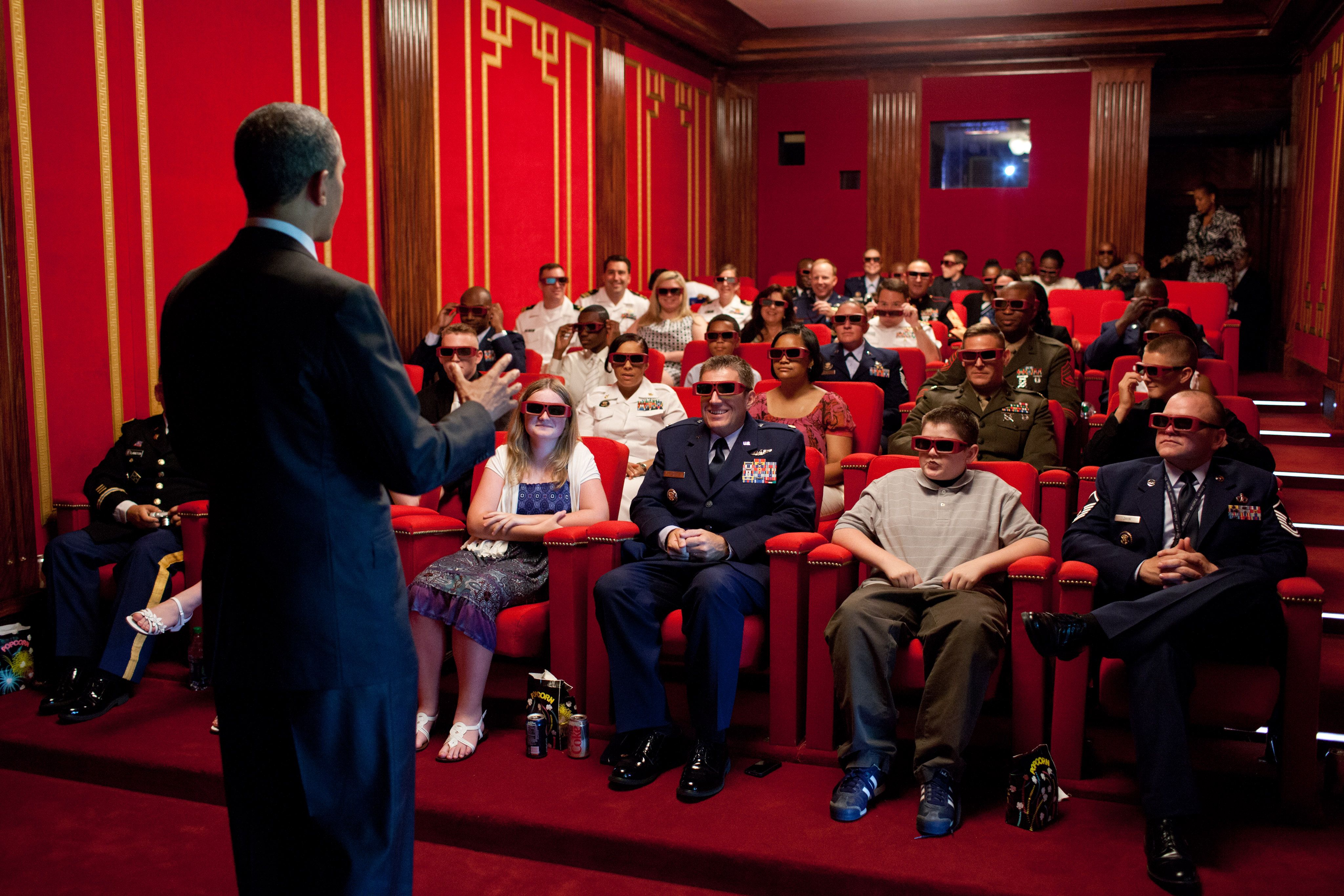 The back of a dark-suited President Obama as he welcomes service members and their families, who are wearing 3D glasses while sitting on red seats, to a screening of "Men in Black 3" in the red-decorated White House Family Theater in 2012. Photo: Pete Souza/The White House via Getty Images