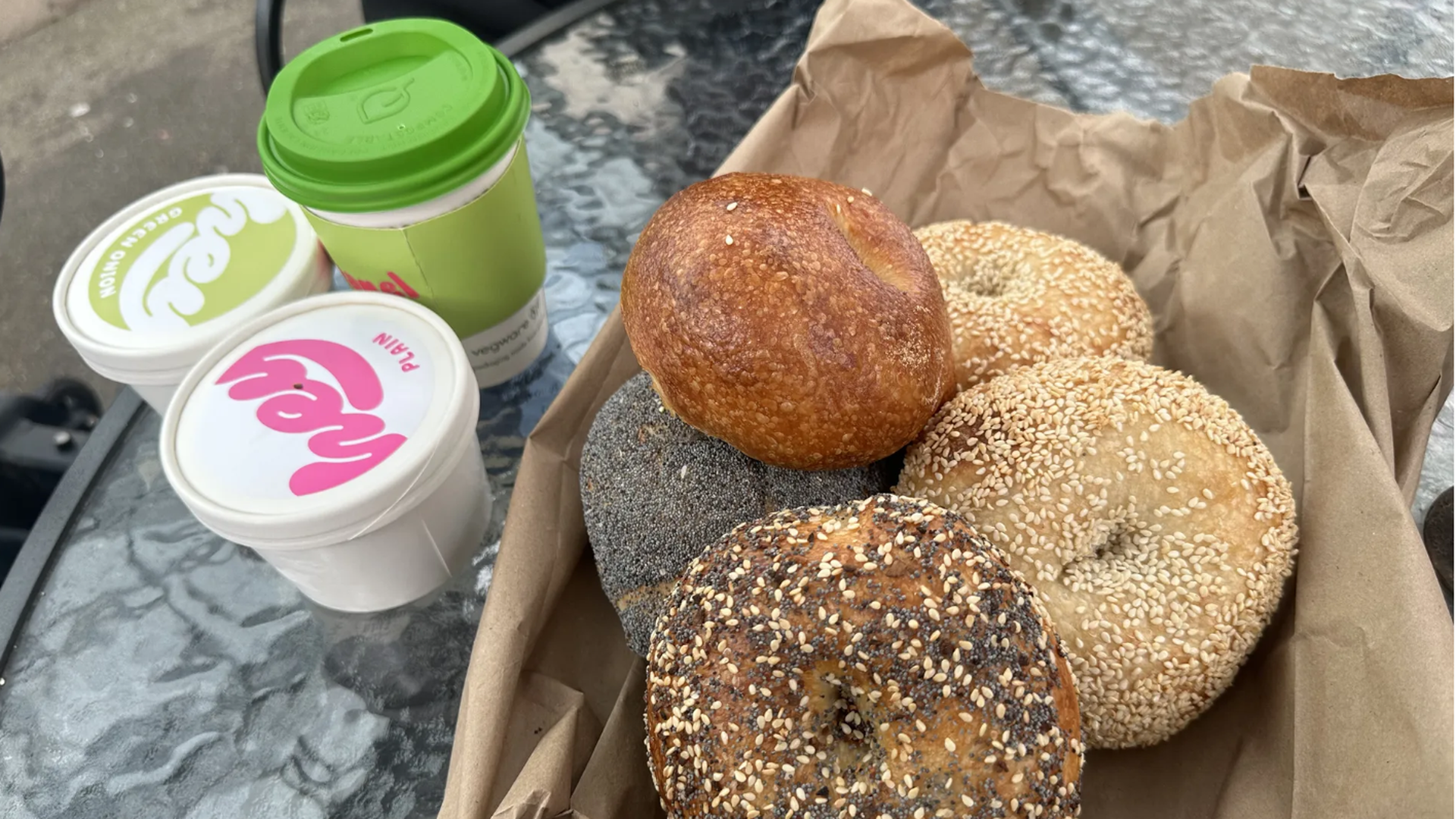 A box of mixed bagels on a table with several drink containers alongside. 
