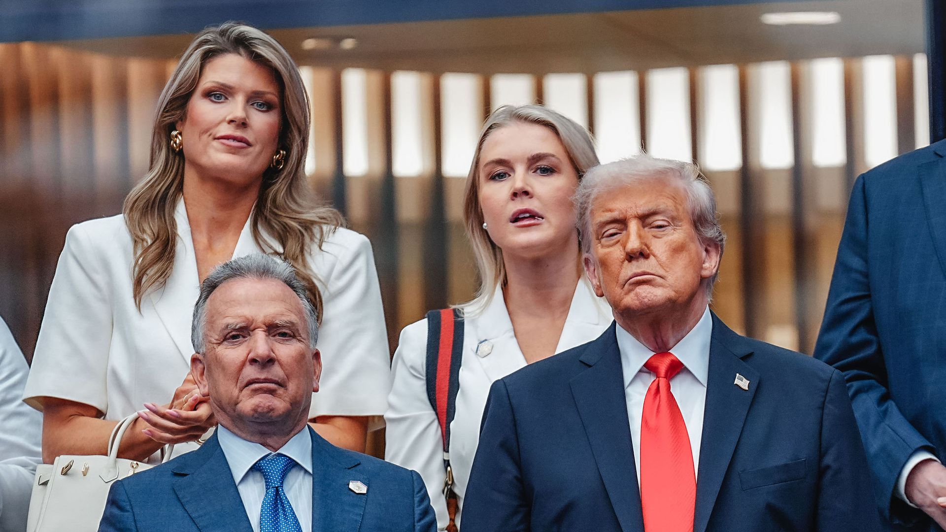 Lindsey Halligan and Karoline Leavitt, both wearing white, stand behind President Trump and Steve Witkoff, both of whom are wearing suits at the U.S. Open.