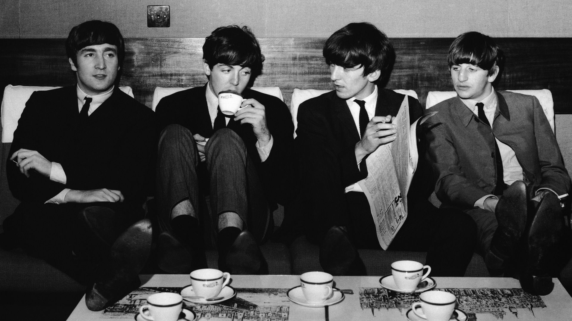 Black and white image of The Beatles on a couch, drinking out of cups