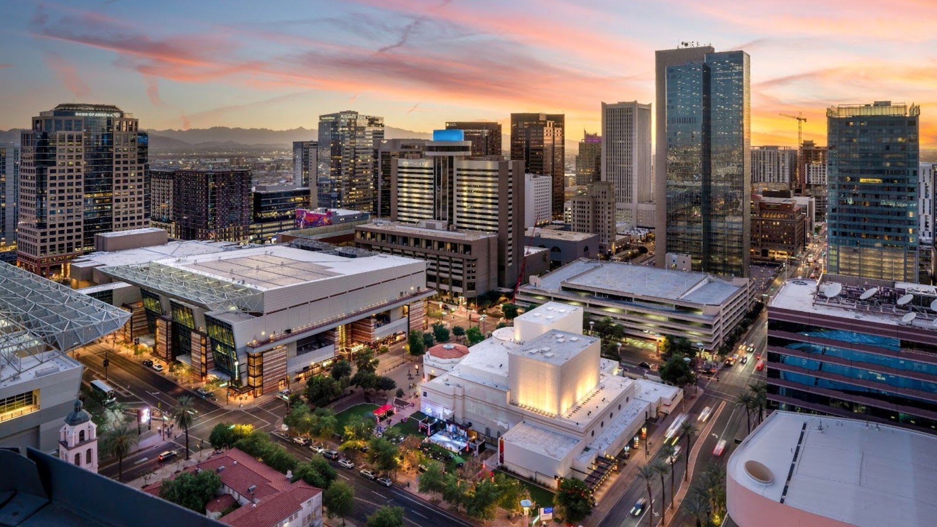 A vibrant sunset casts warm light over the Phoenix skyline, highlighting modern high-rises, the convention center and city streets below.