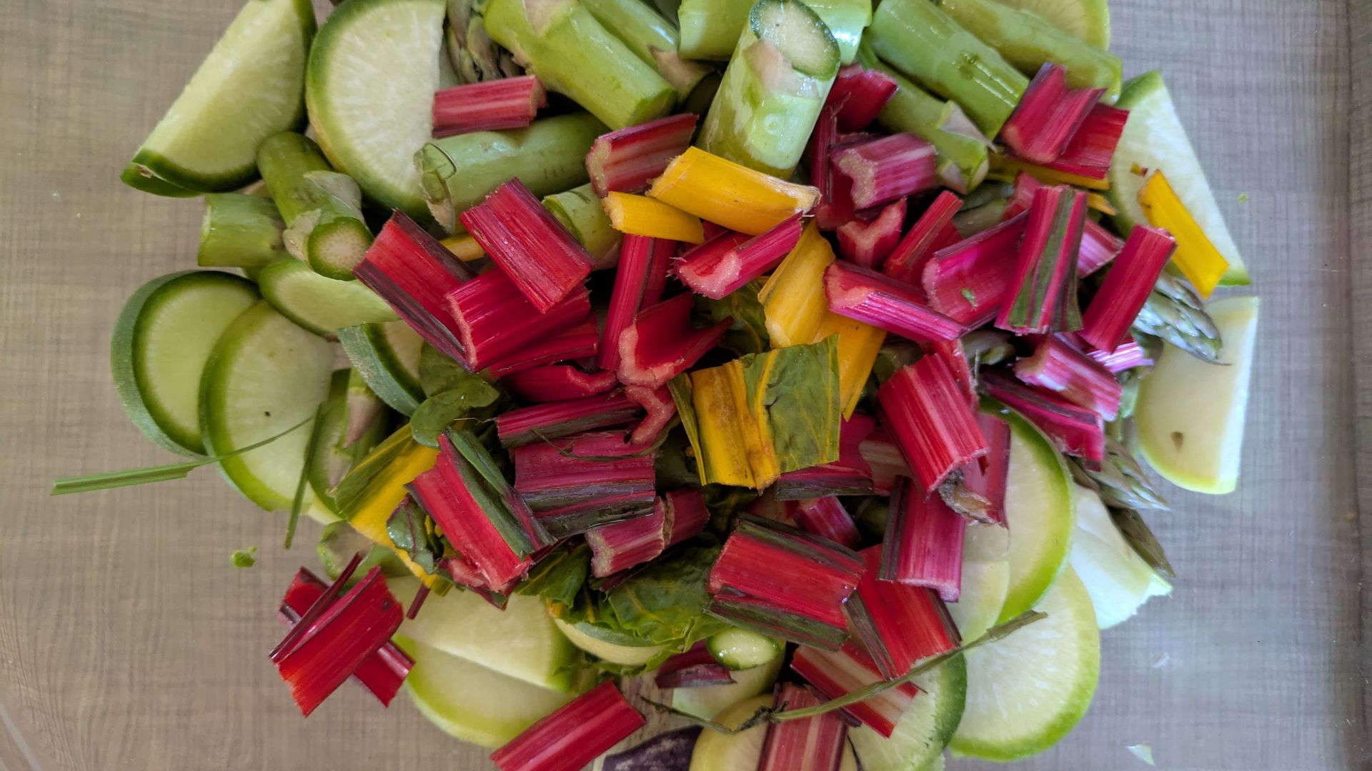 Assorted chopped rhubarb stalks in red, pink, green and yellow, with lime wedges and rounds on a wooden cutting board.