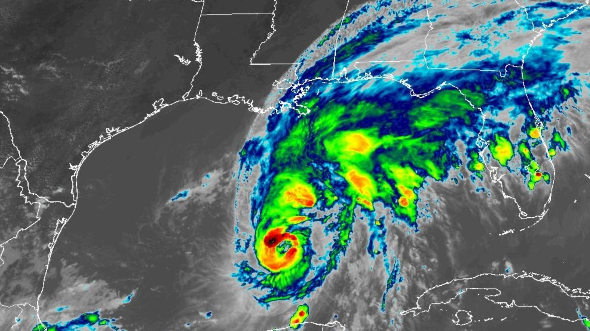 Satellite weather image showing a tropical cyclone in the Gulf with a defined eye and spiraling rain bands; heavy rainfall shown in green, yellow, and red near the Gulf Coast.