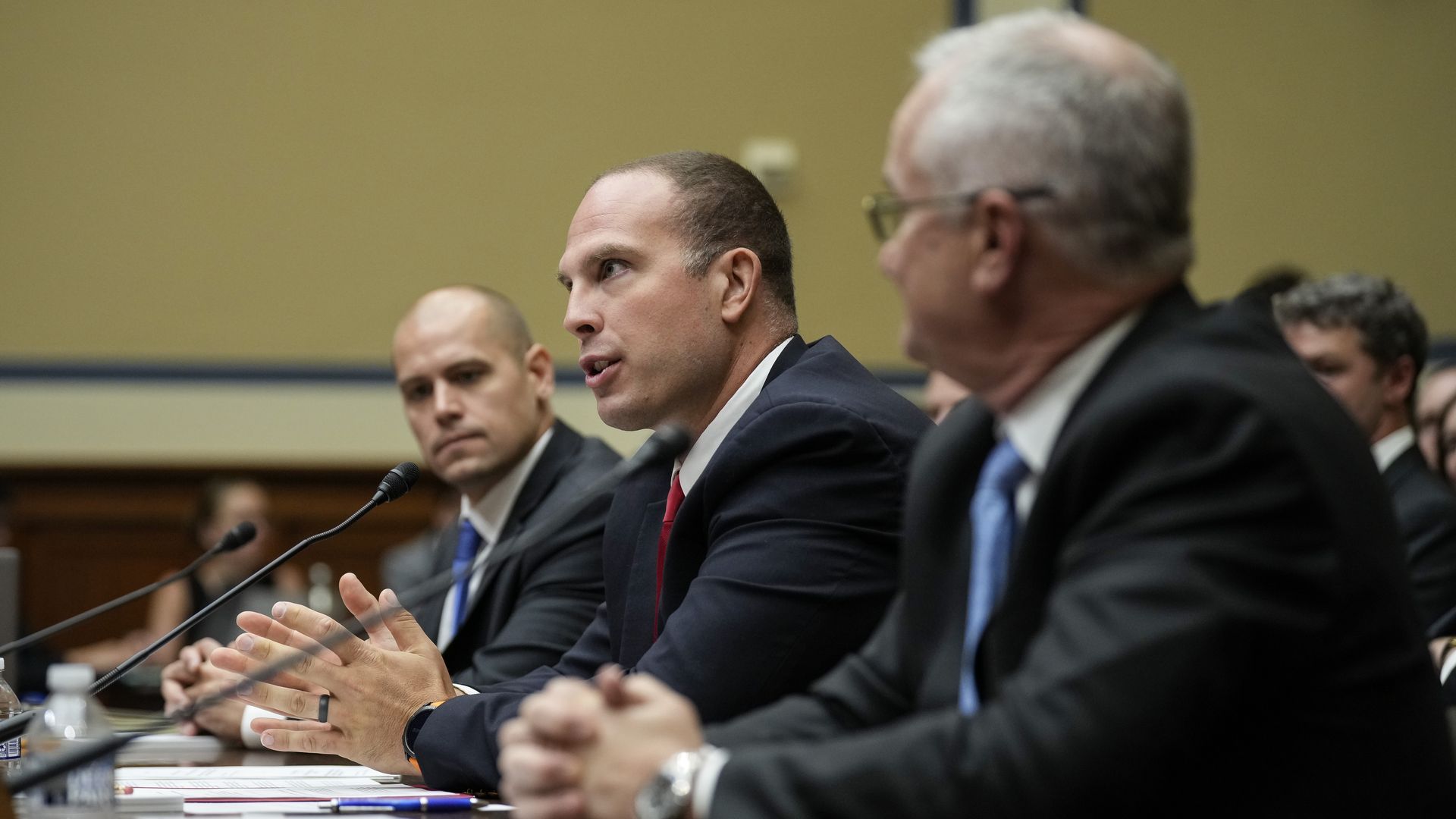 Three men at a Congressional hearing. The one in the middle is speaking