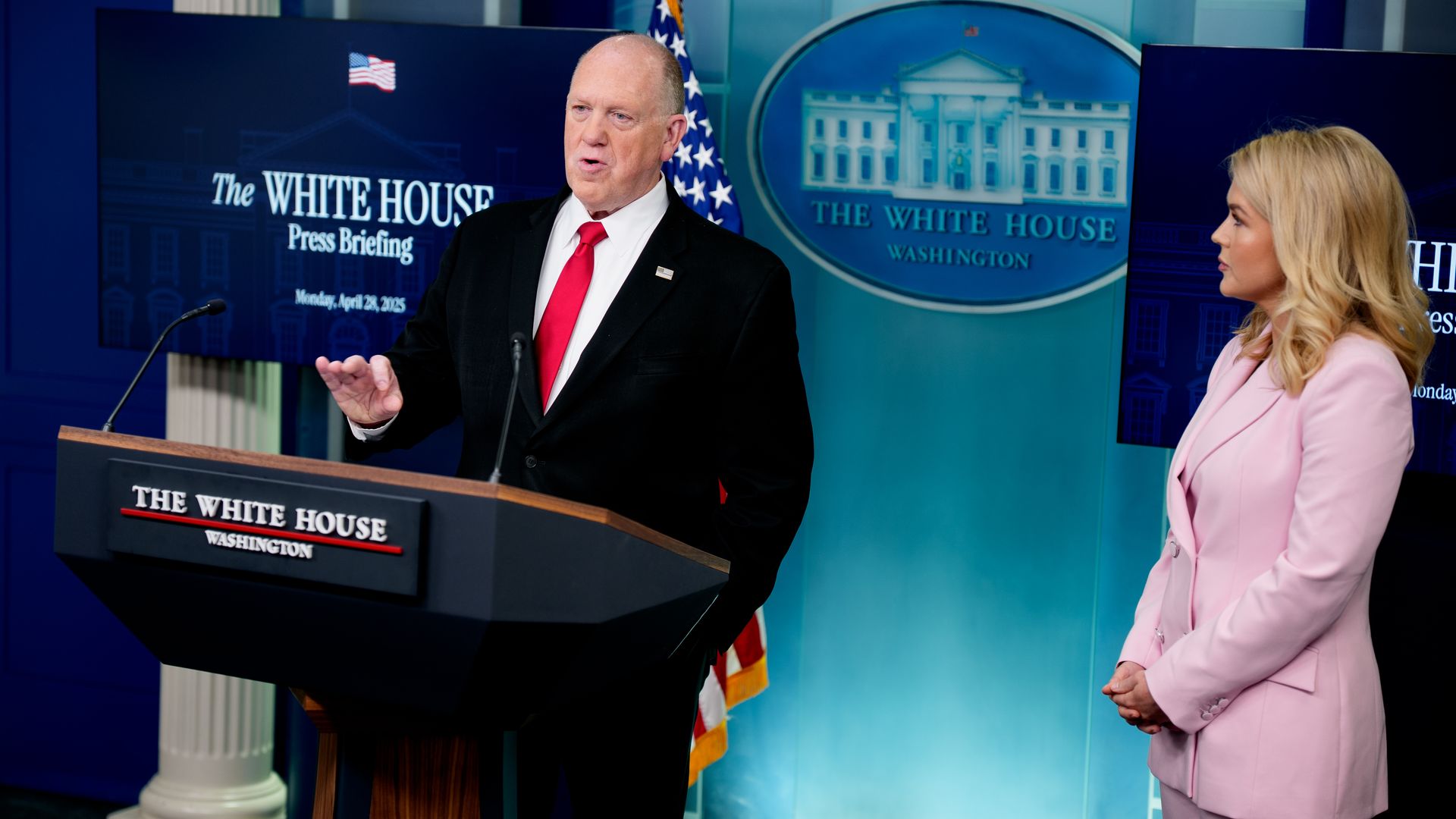 Tom Homan speaks in the White House briefing room from behind a lectern while Karoline Leavitt looks on/