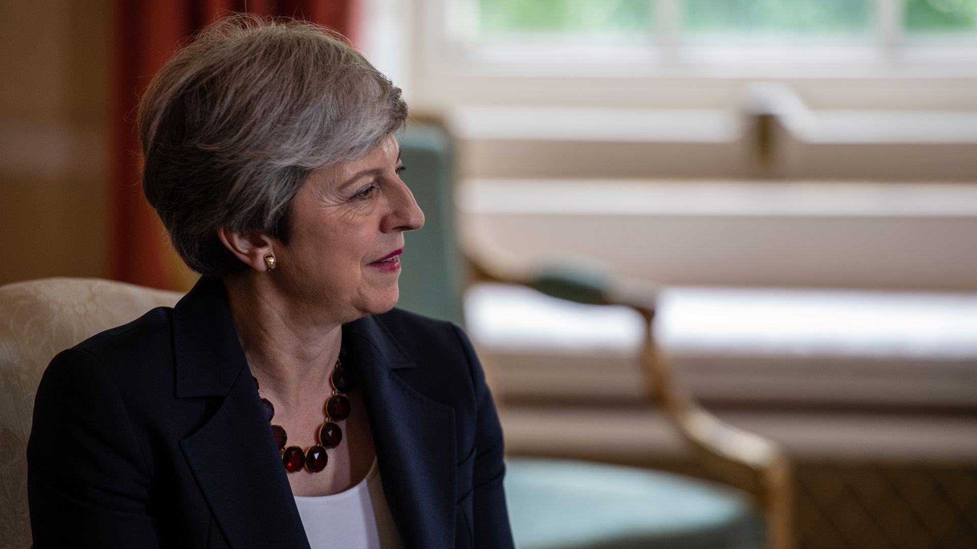 In this image, Theresa May sits and listens to someone speaking to her right.