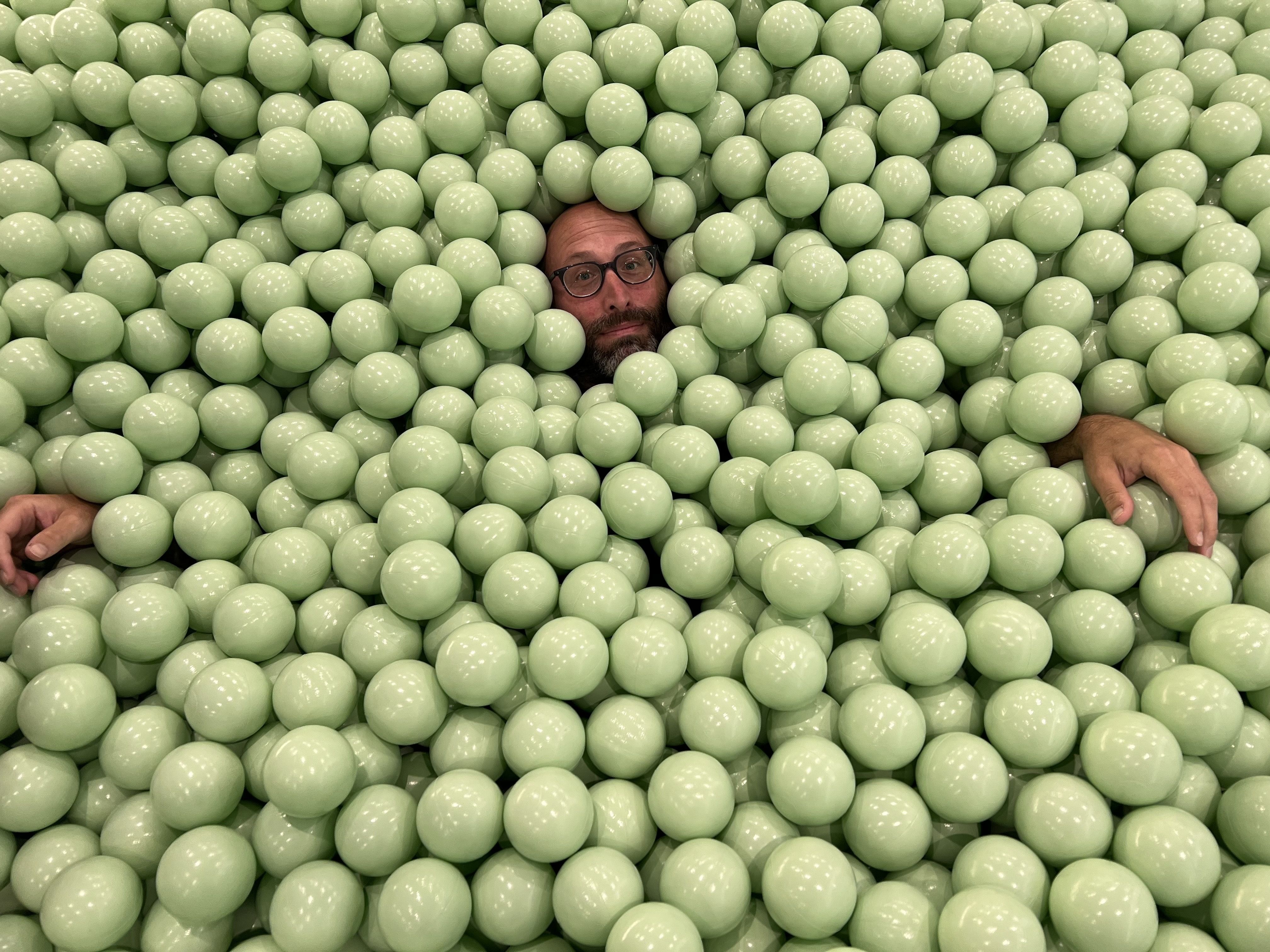 Photo of a man submerged in plastic balls in a ballpit. 