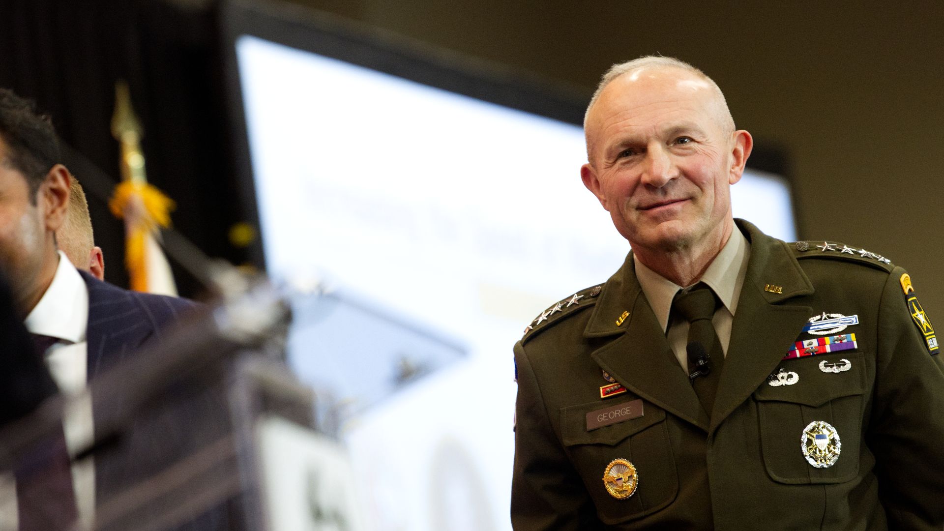 Gen. Randy George, a man in U.S. Army uniform, smiles as he walks off a stage at a defense conference. A large electronic screen is seen behind him.