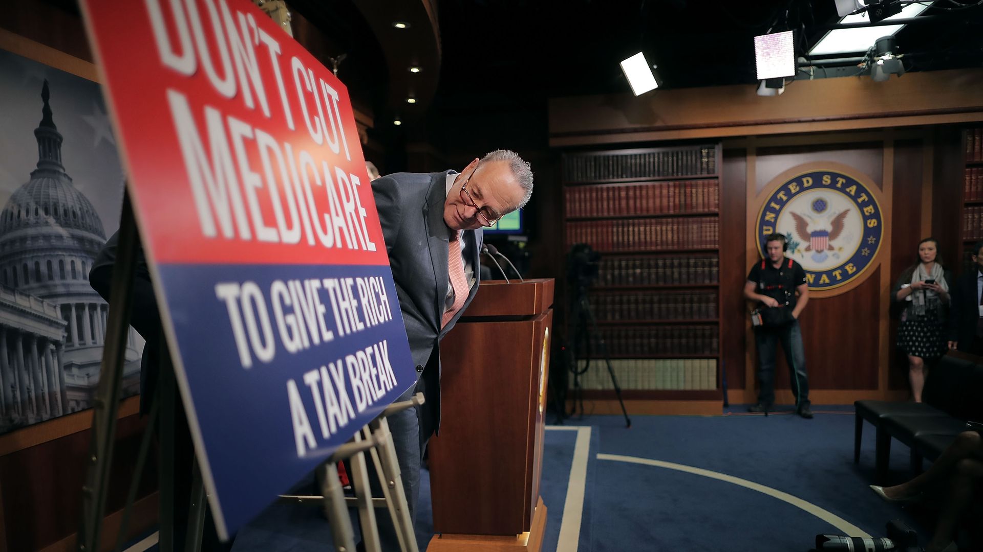 Chuck Schumer leaning over to look at a sign about health care and taxes