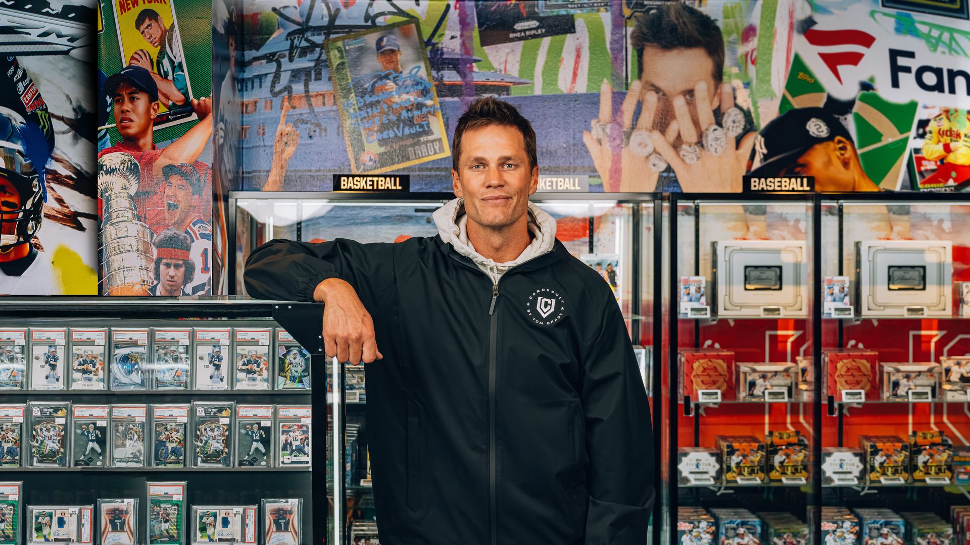 Tom Brady standing in front of displays of trading cards and sports memorabilia. 