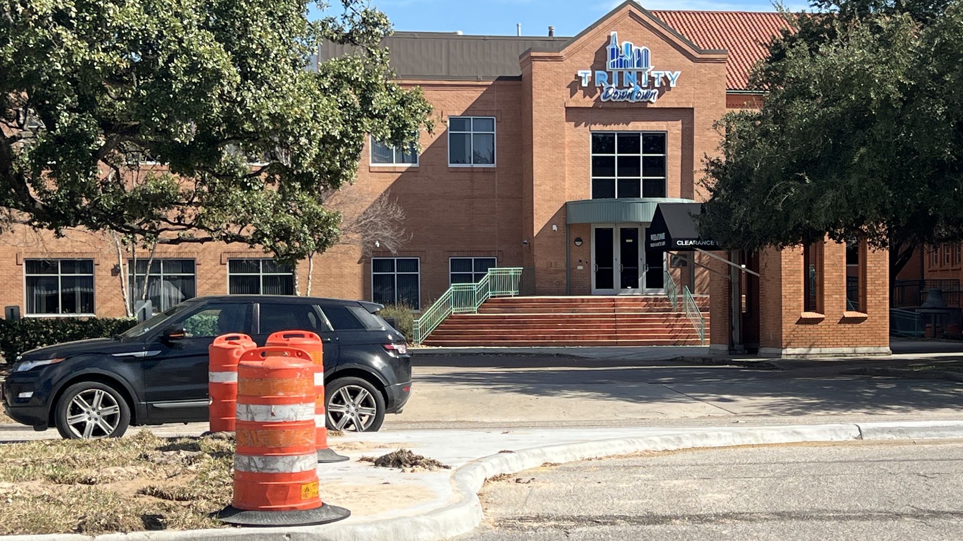 Orange traffic cones sit on a median with Trinity Downtown in the background