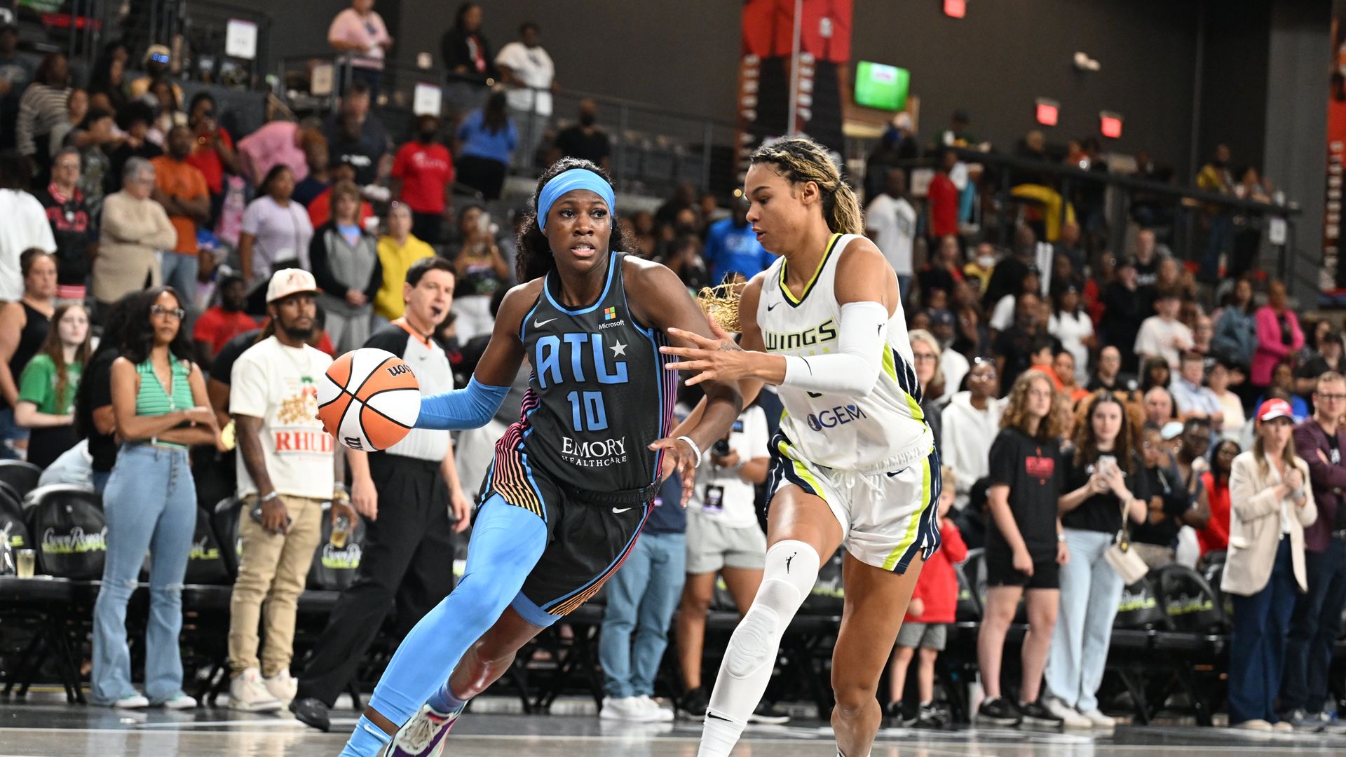 A woman in a basketball jersey dribbles past a defender in a white uniform