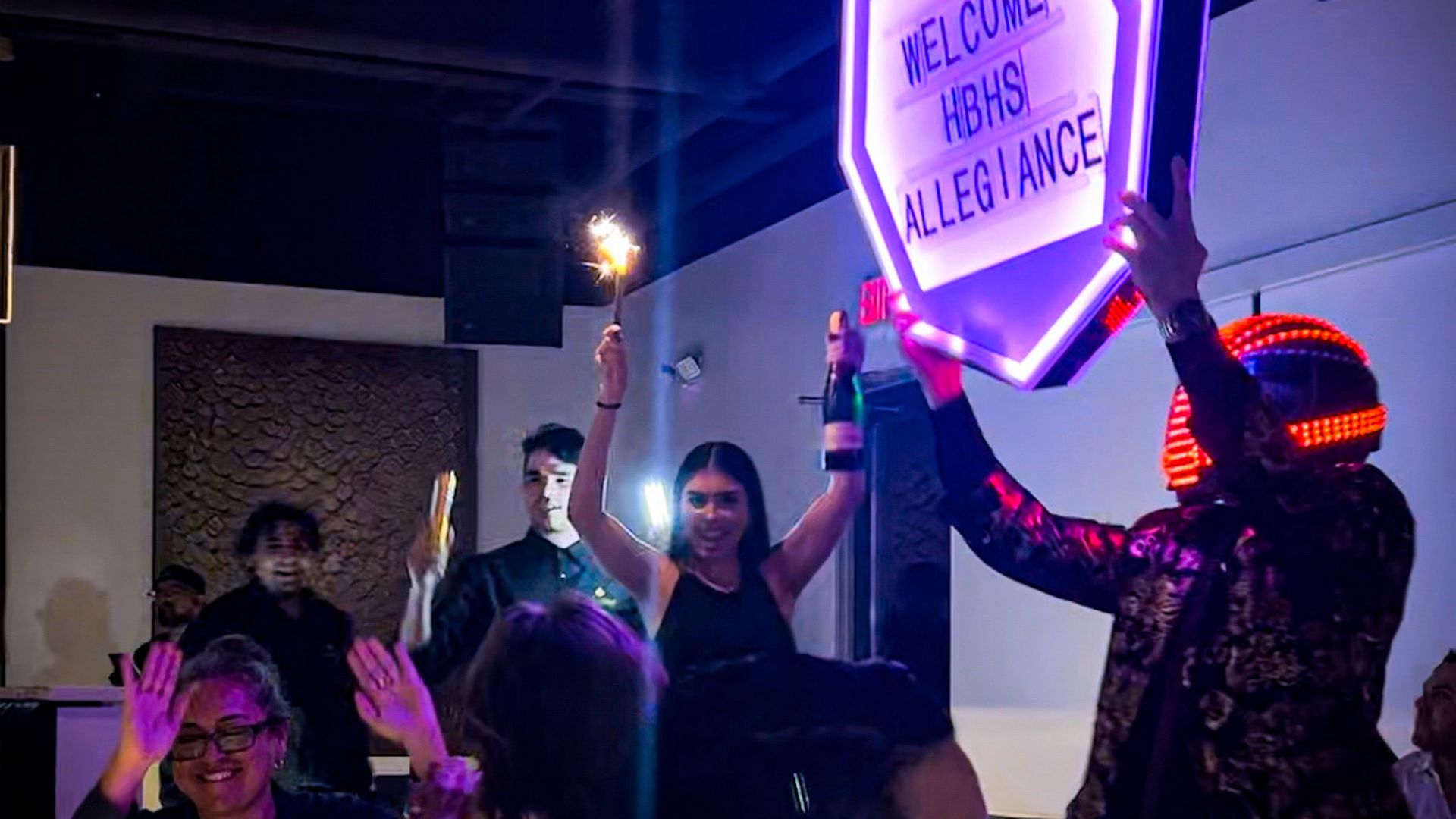 Restaurant staff present food and drinks to a table with sparklers and illuminated signs.