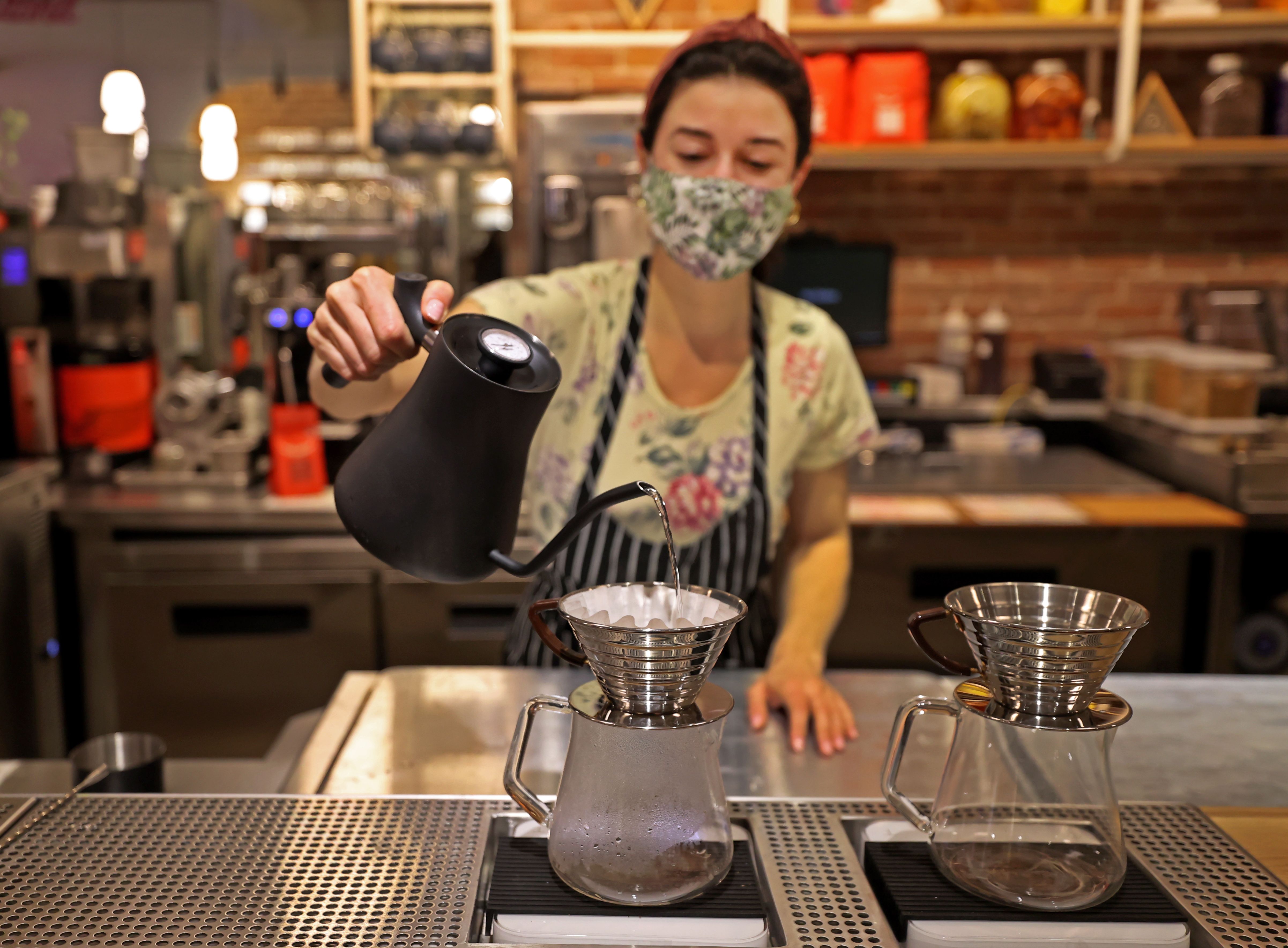 A cafe worker pours hot water over coffee grounds.