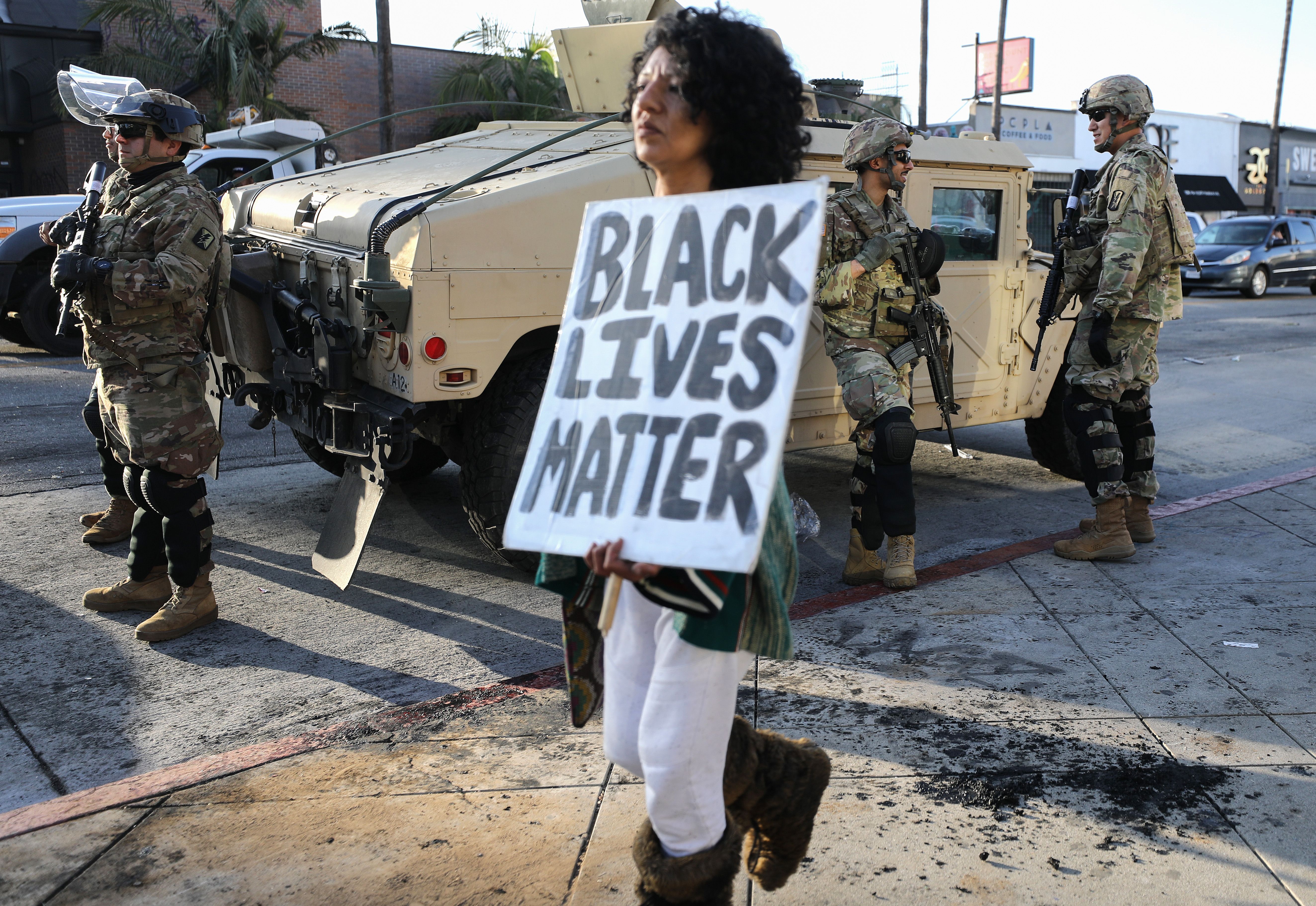 A woman carries a 'Black Lives Matter' sign past U.S. National Guard troops in Los Angeles