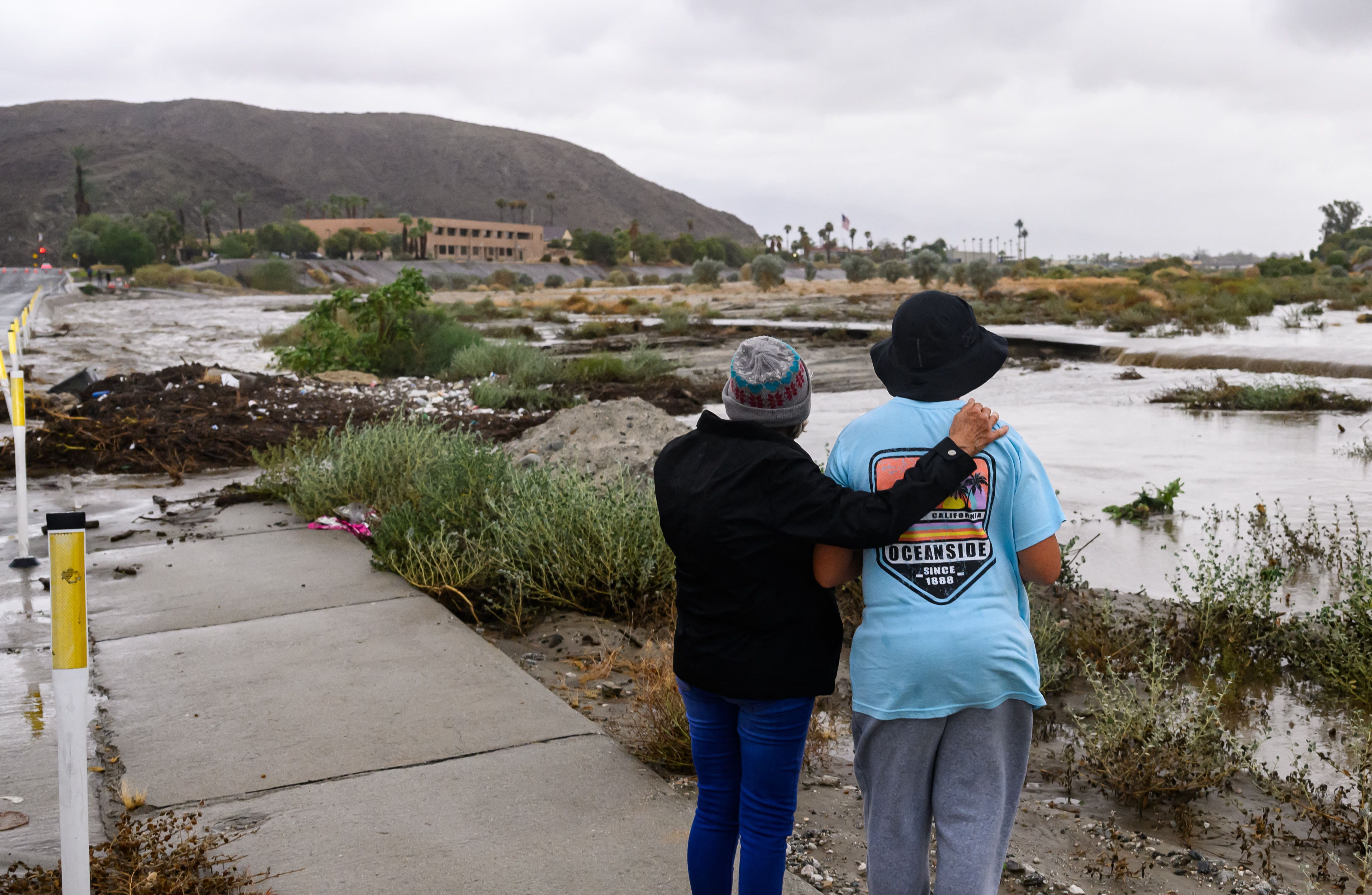 Pedestrians look towards a flooded waterway as tropical storm Hilary makes landfall in Rancho Mirage, California on August, 20, 2023. Heavy rains lashed California as Tropical Storm Hilary raced in from Mexico, bringing warnings of potentially life-threatening flooding in the typically arid southwestern United States.