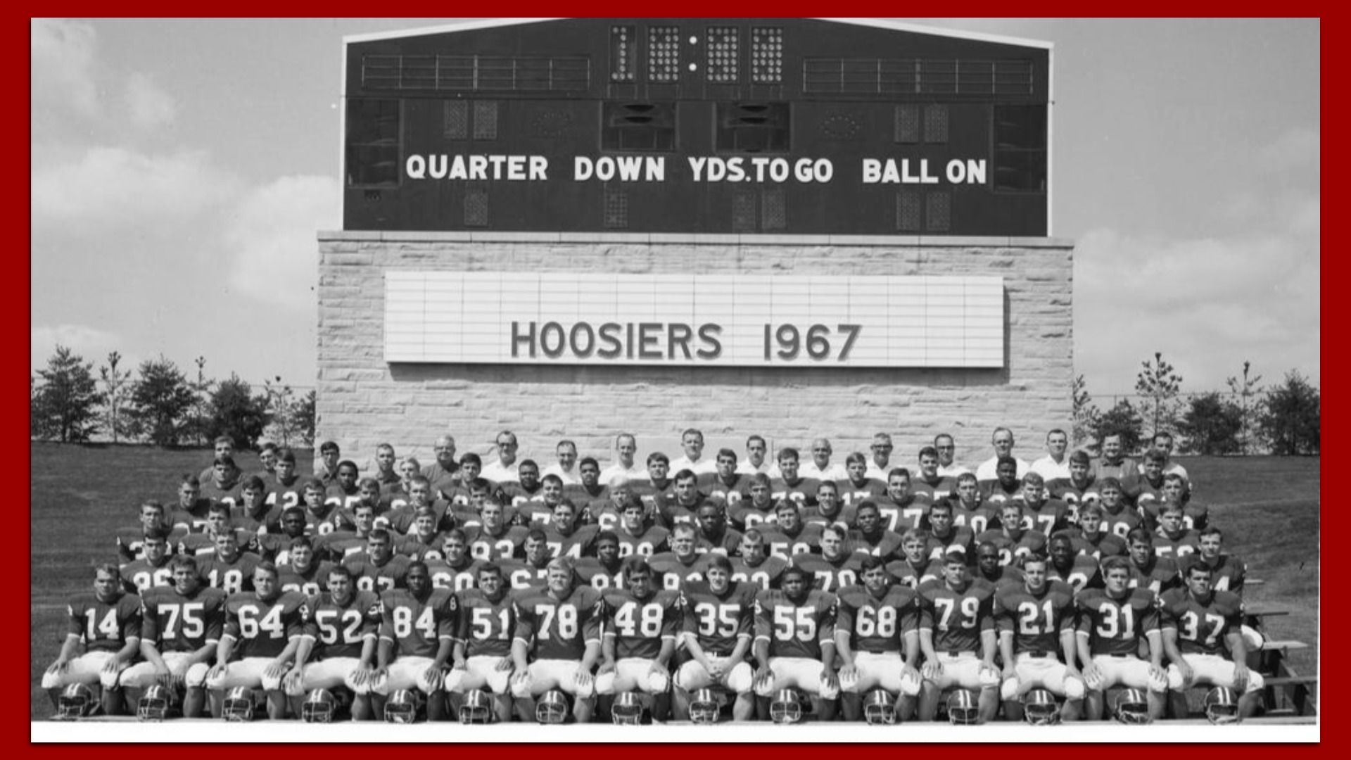 Black and white photo of the 1967 Hoosiers football team in uniforms posing in front of a scoreboard showing "HOOSIERS 1967".