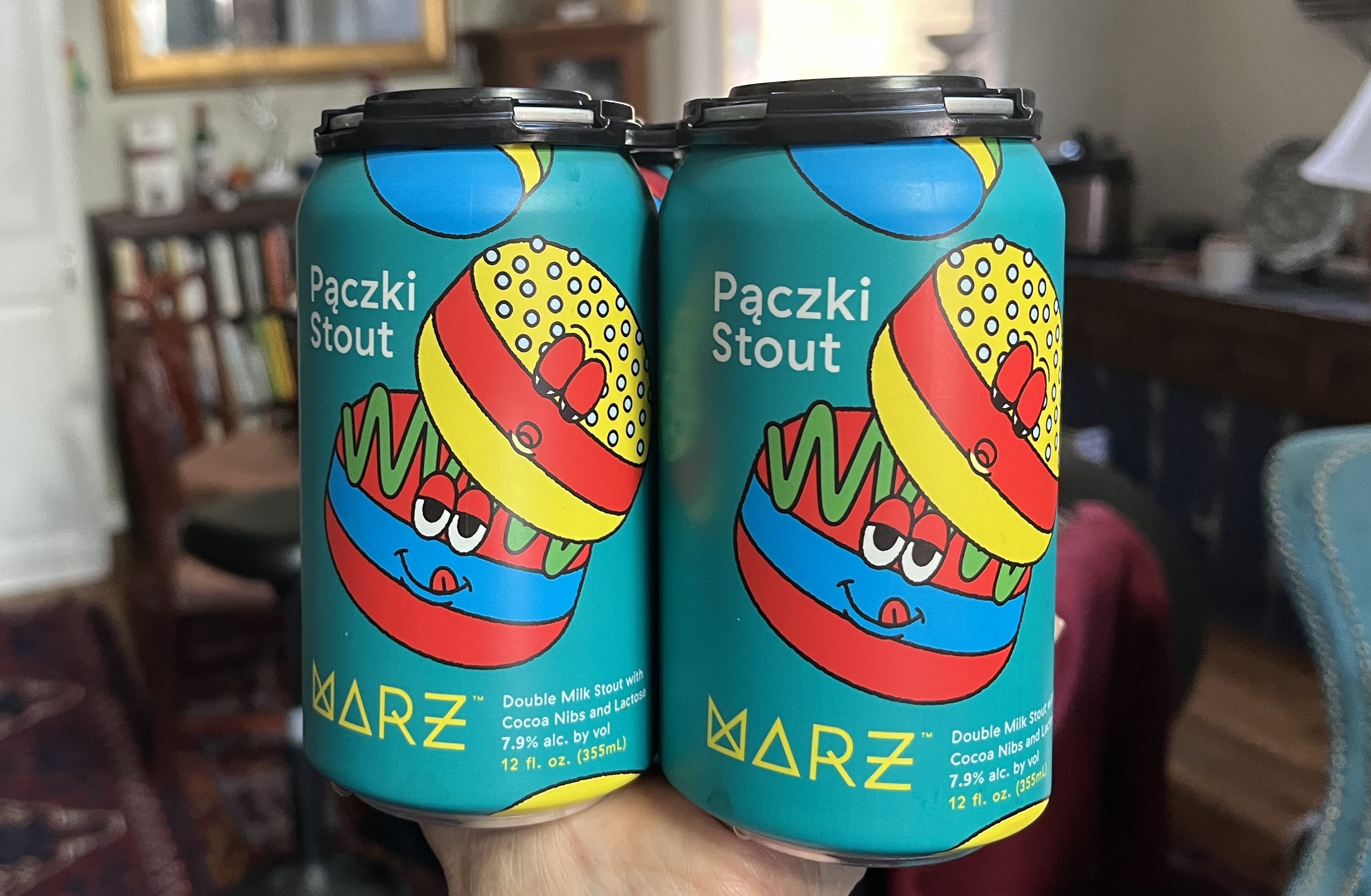 Two blue cans of Pączki Stout beer with colorful donut cartoon art, labeled as double milk stout with cocoa nibs and lactose, 7.9% alcohol, 12 fl. oz., from Marz brewery.