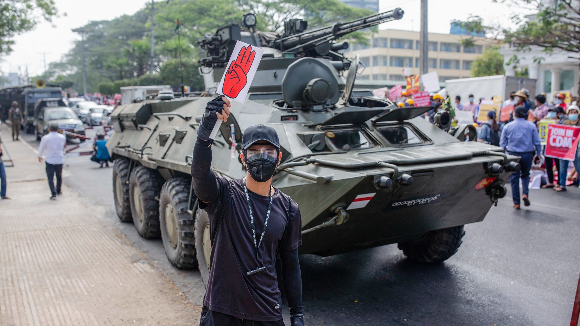 A protester holds a placard with a three-finger salute in front of a military tank parked aside the street in front of the Central Bank building during the demonstration.  