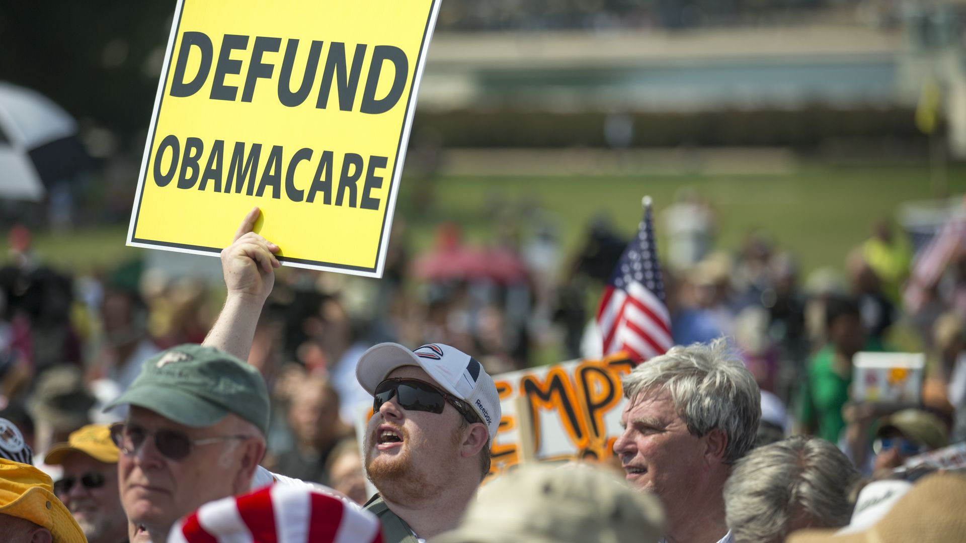 A crowd of people, with a man holding a sign that says "Defund Obamacare" 