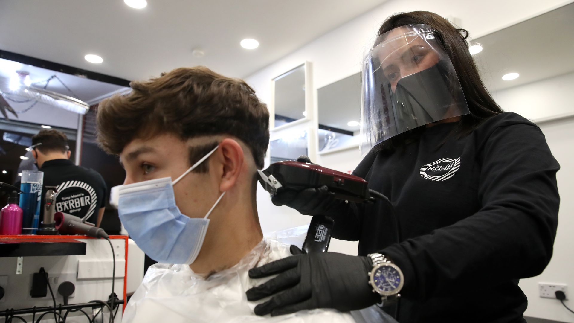 A hair stylist with a mask and face shield on cutting the hair of a boy with a face mask on