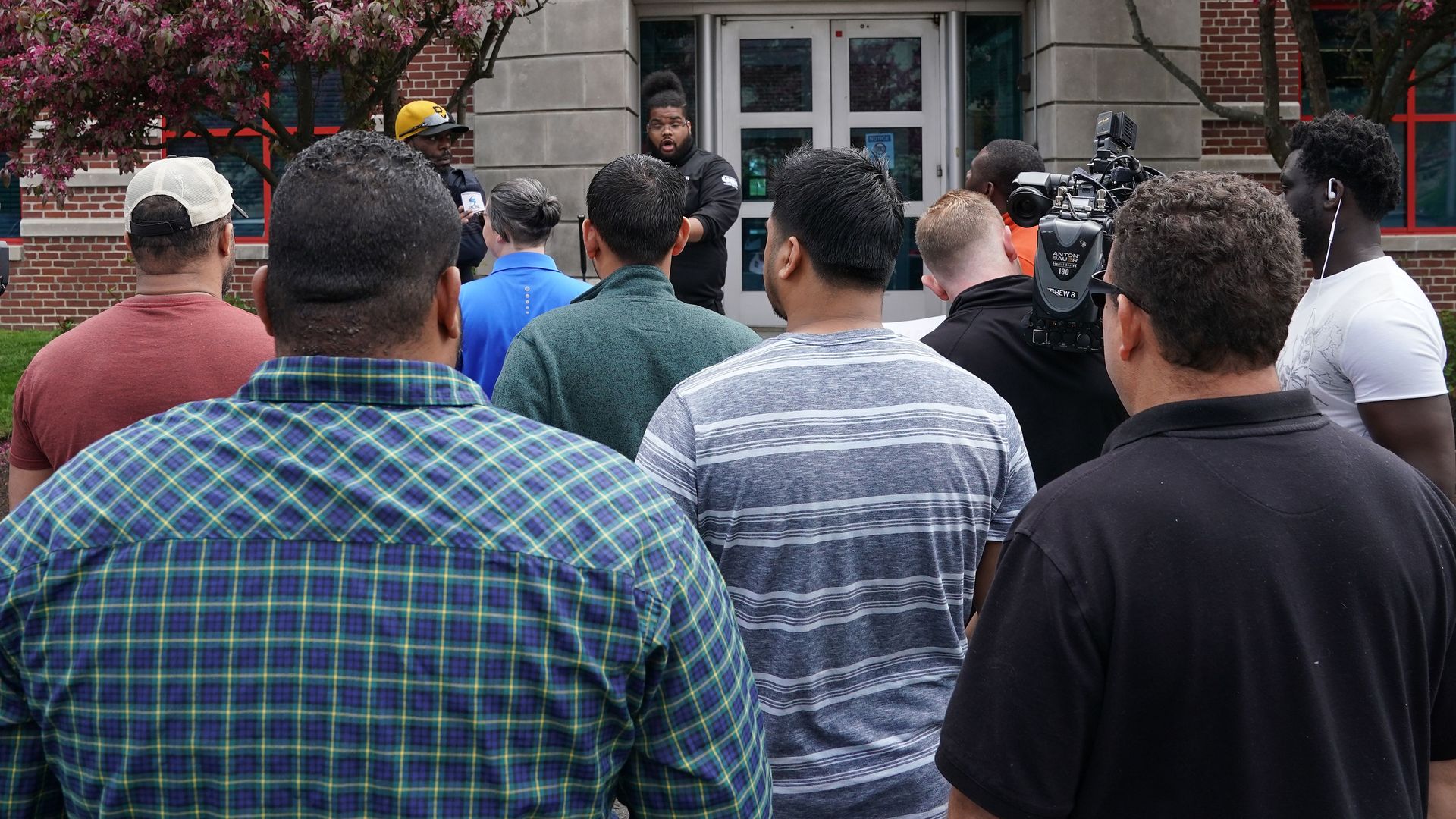 A line of men stand, facing away from the camera