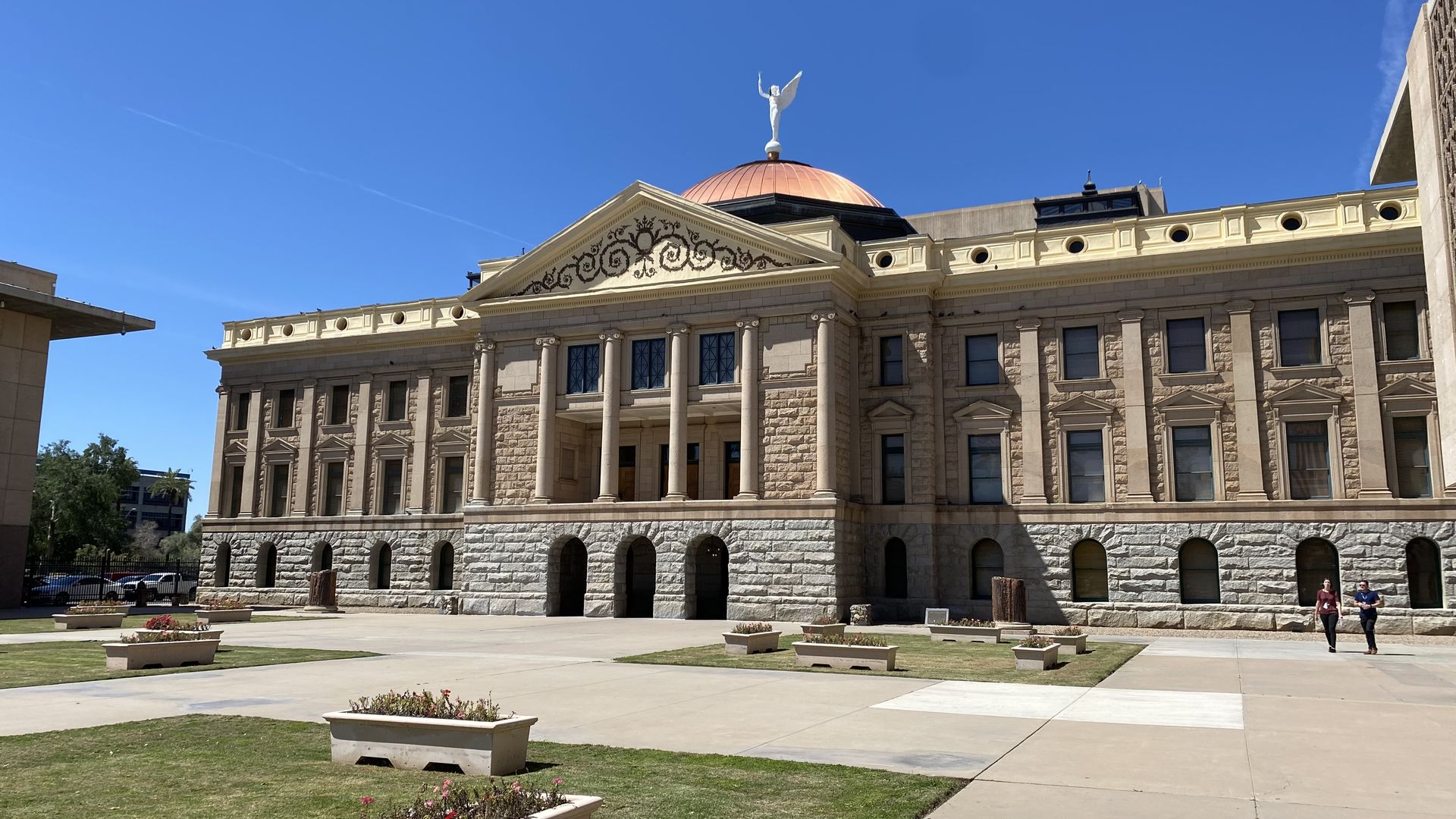 A classical building topped with a copper dome and an angel statue. 