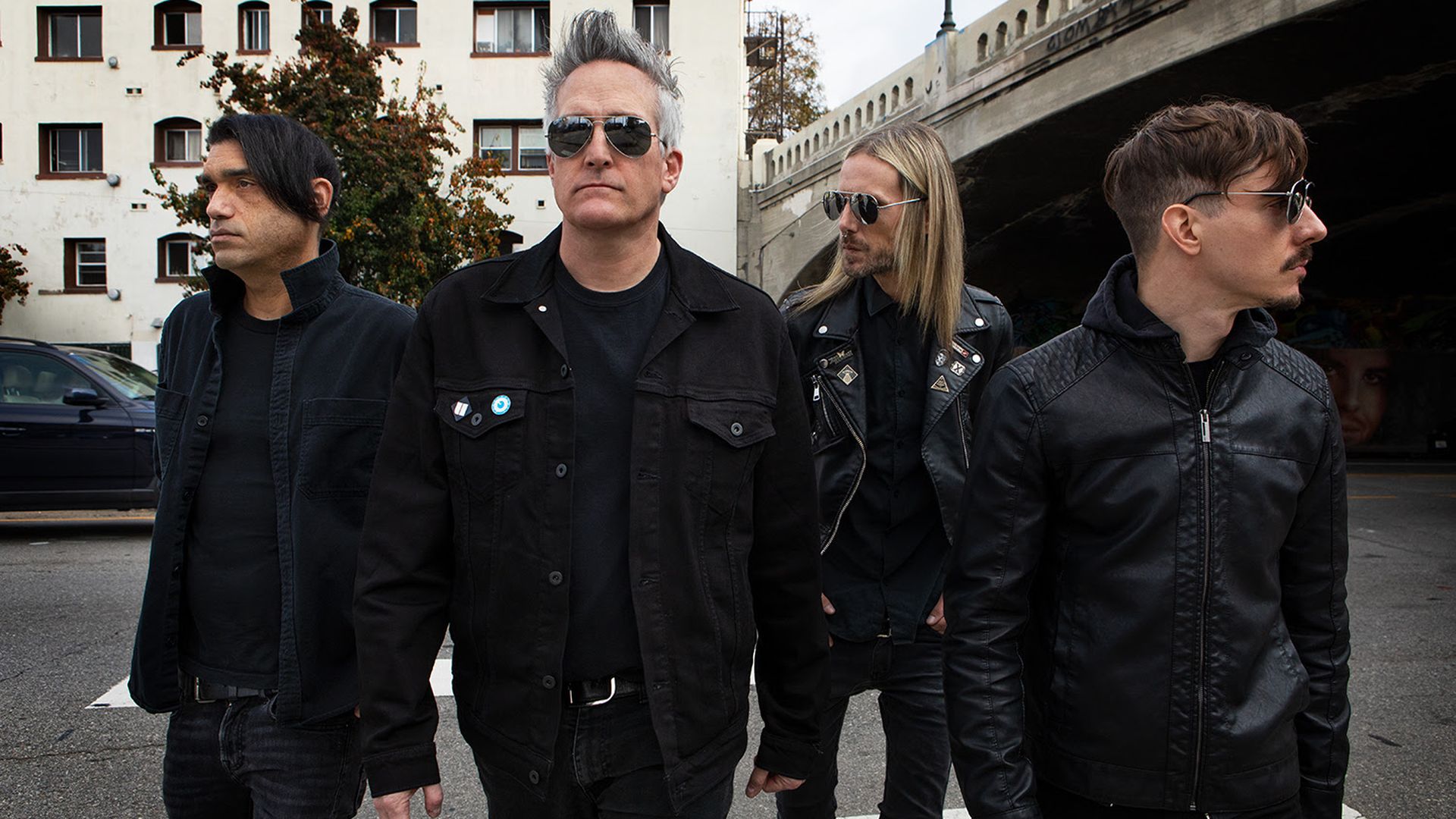 Four men dressed in all back walk on the street together.