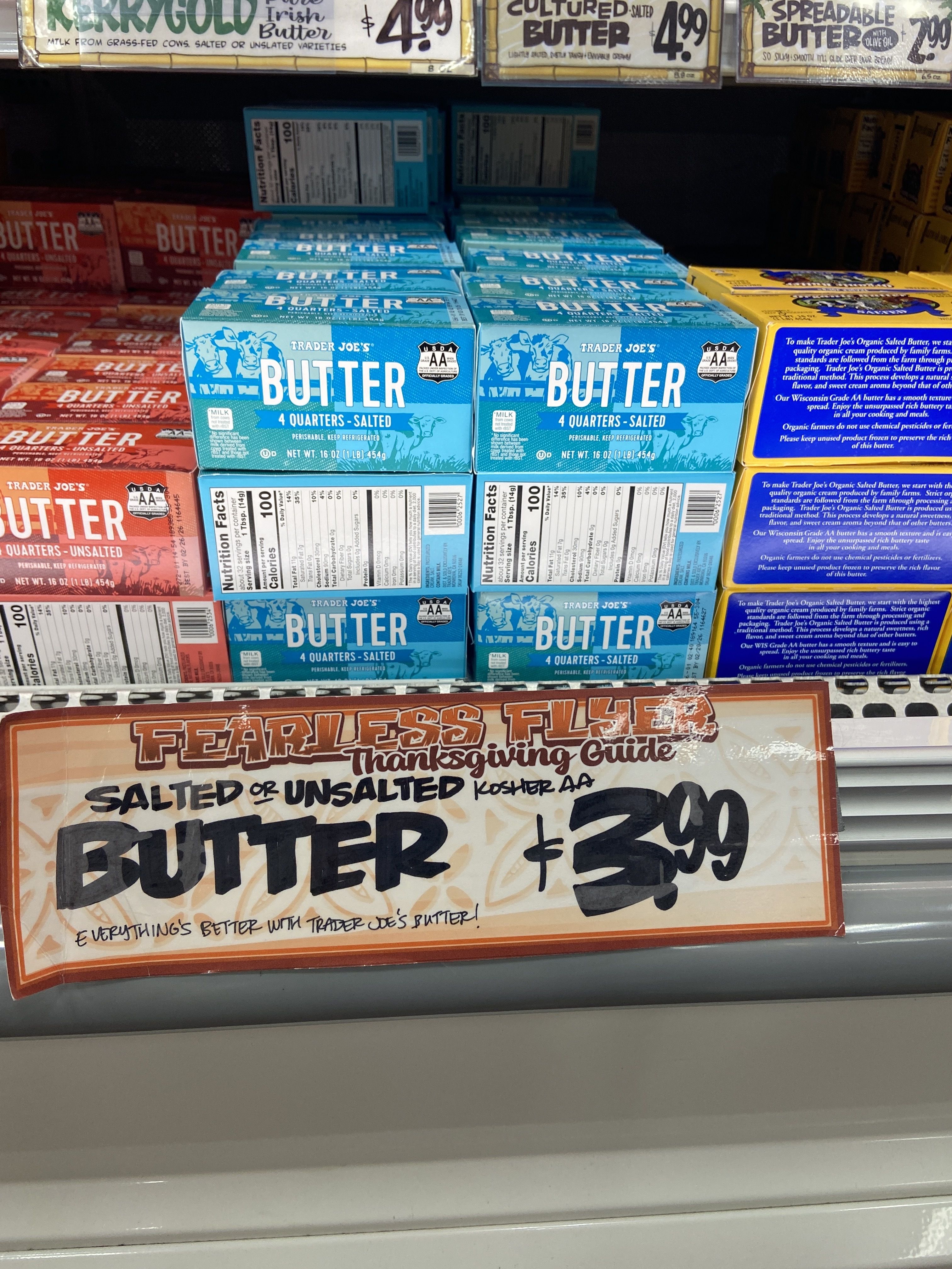 Shelf display of Trader Joe's butter in blue (salted) and red (unsalted) boxes with a sign reading "Butter salted or unsalted $3.99" in a store freezer.
