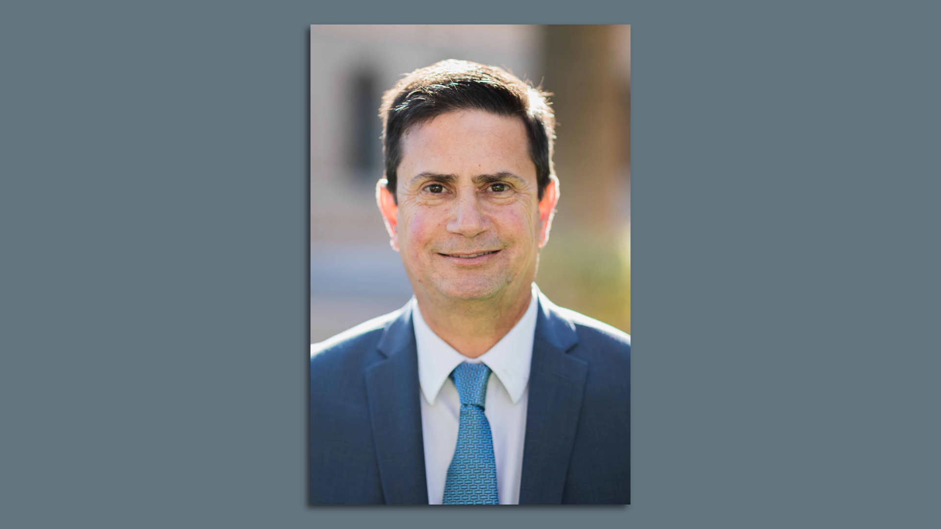 A mug shot of a man with short brown hair in a blue jacket, white shirt and blue tie.