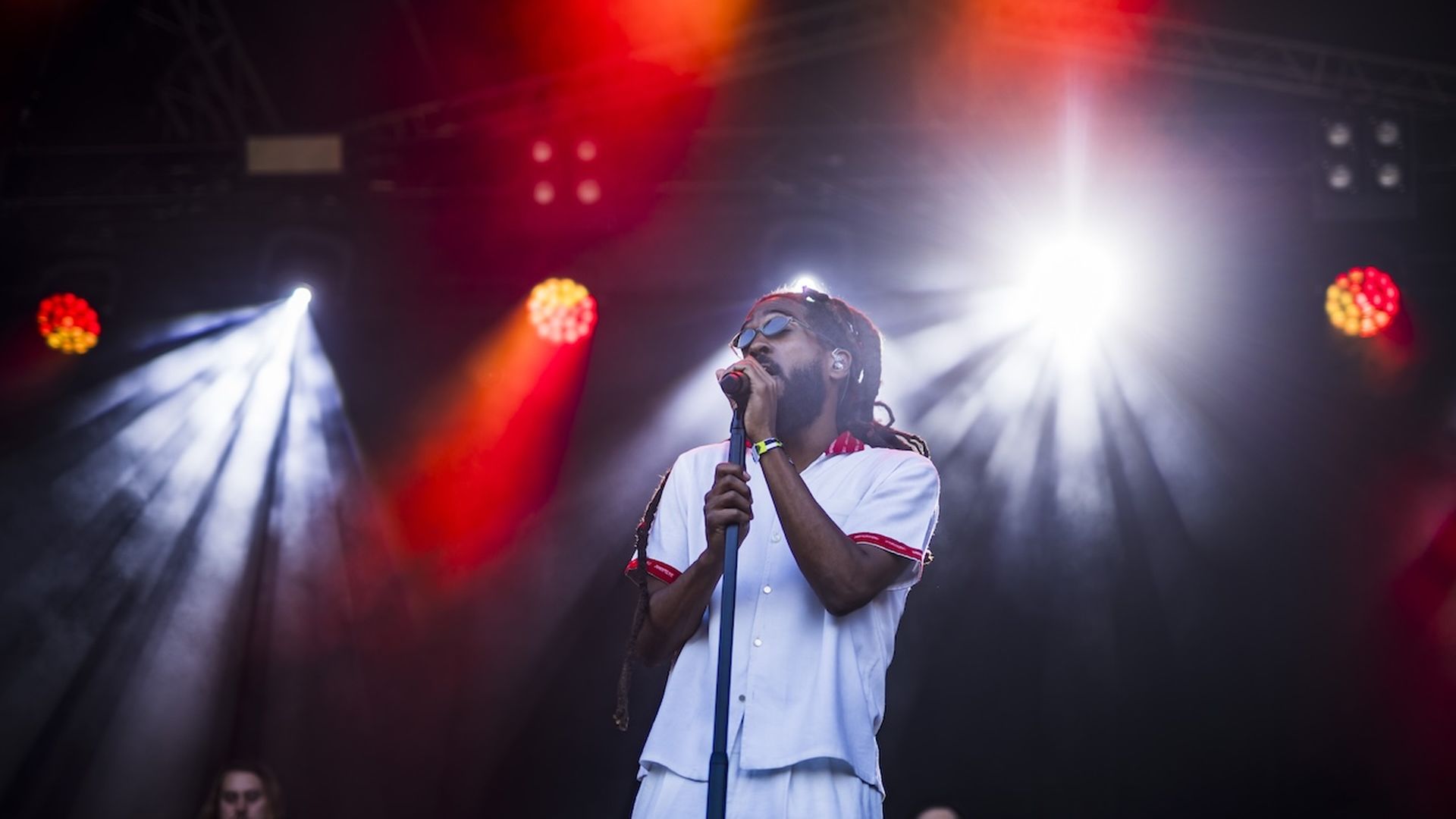 A photo of a person holding a microphone and stand on a stage with white and red spotlights.