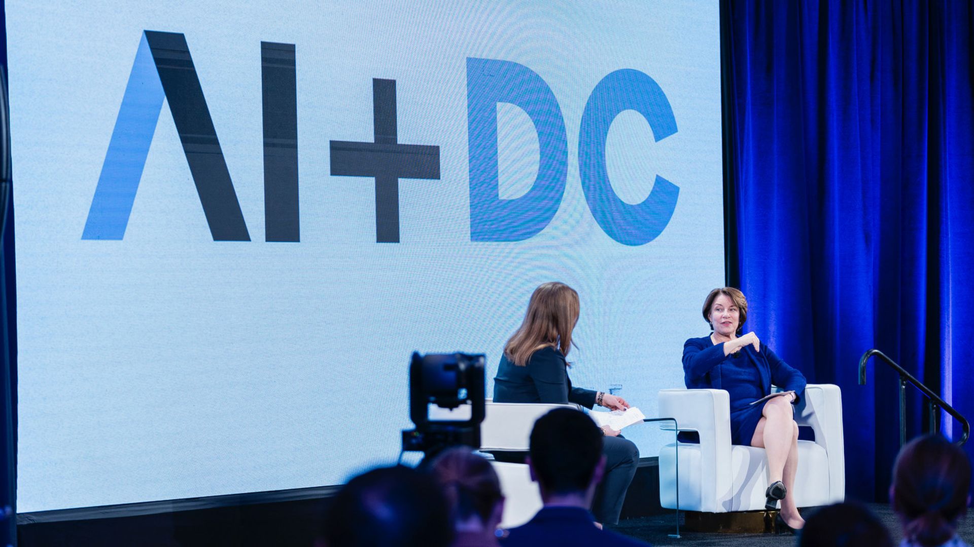 Two people seated on a stage under an AI+DC sign